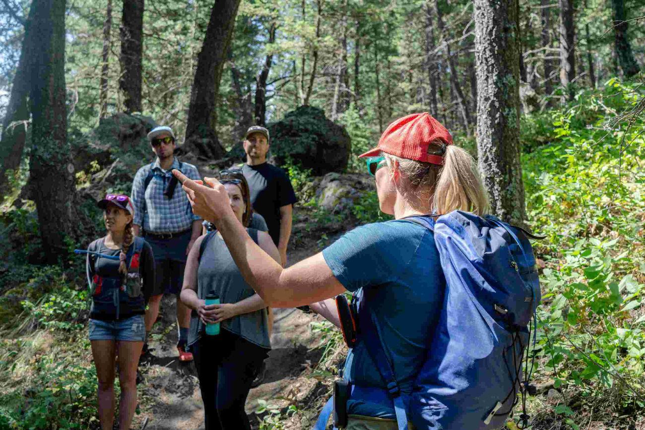 Guide speaking to hikers gathered on a wooded trail.