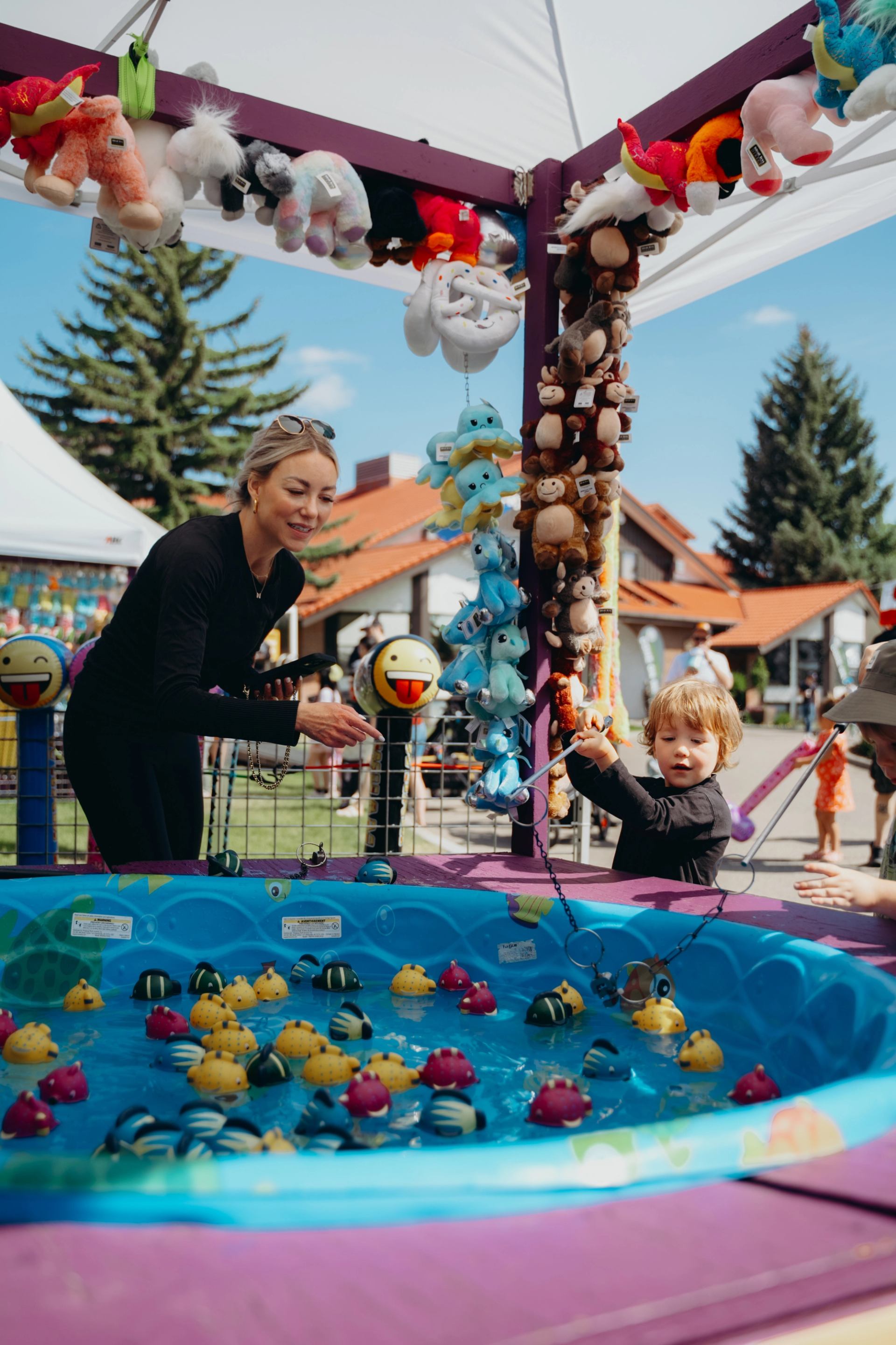 Child playing a fishing game at a carnival booth decorated with plush toys.