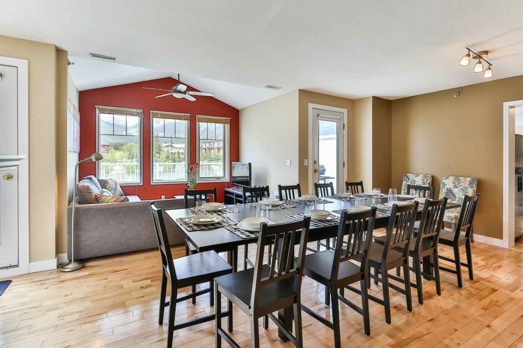 Dining area with long table set for 12, hardwood floors, and bright windows.