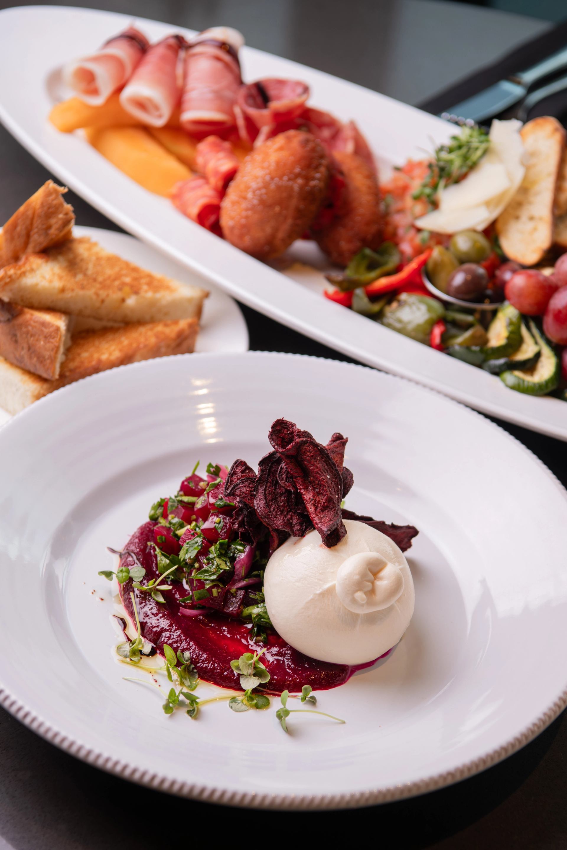 Burrata with beets and greens beside a platter of meats, vegetables and bread.