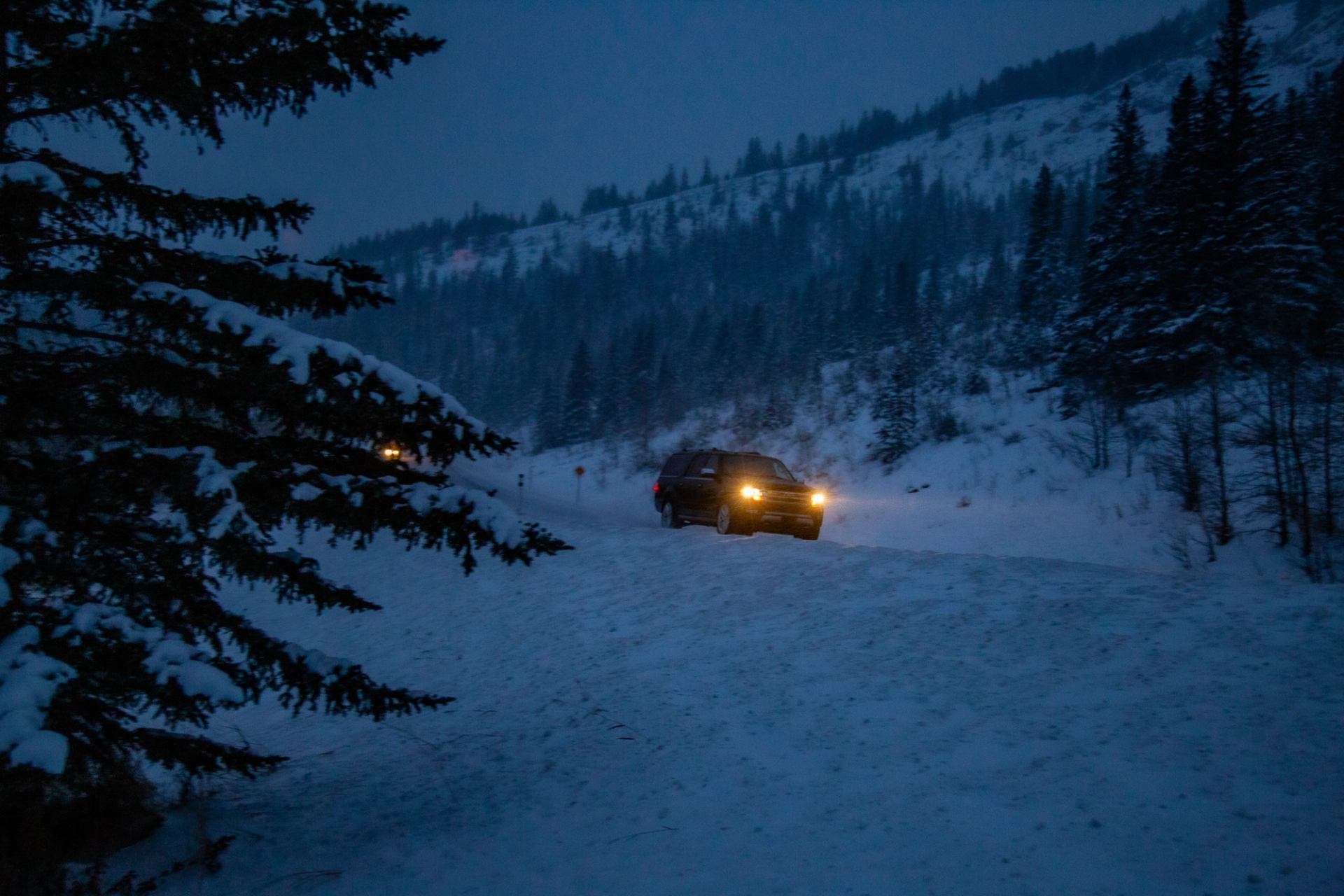 Vehicle with headlights on a snowy mountain road at dusk during a winter adventure.