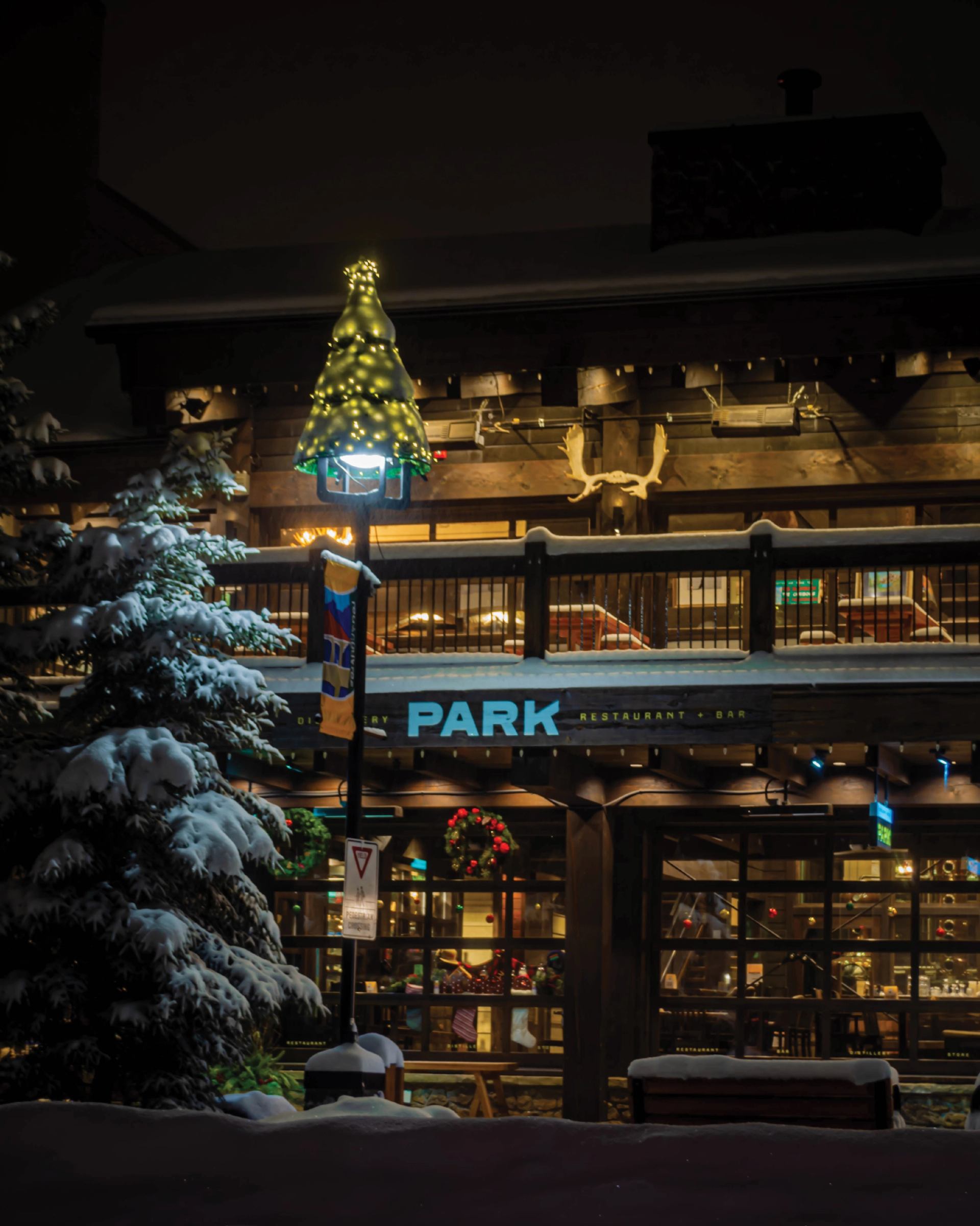 Exterior of PARK Distillery lit warmly at night with snow-covered trees.