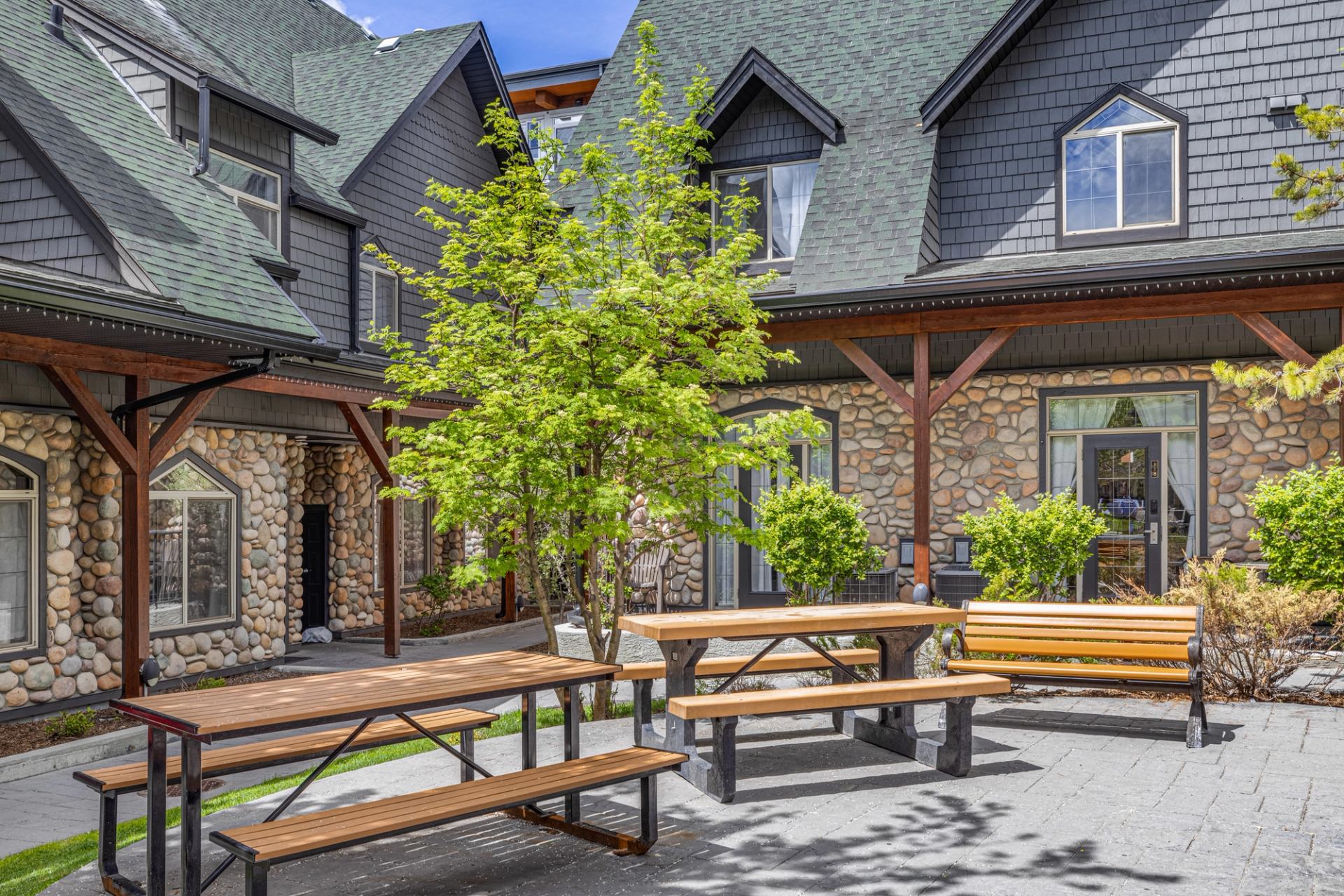 Courtyard with picnic tables, a bench and trees beside stone-clad buildings.