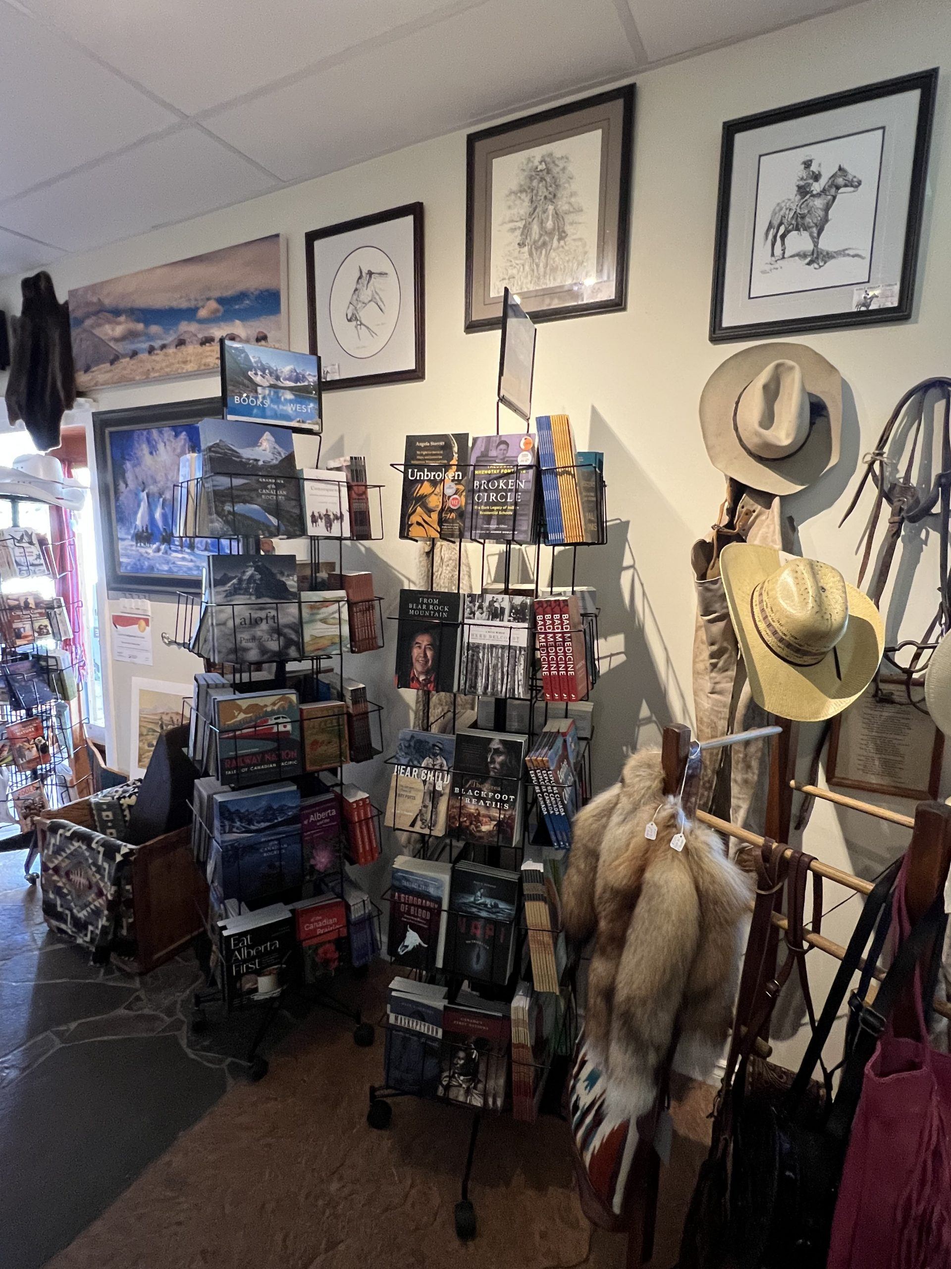 Bookstore corner with rotating book racks, cowboy hats, framed art and hanging furs.