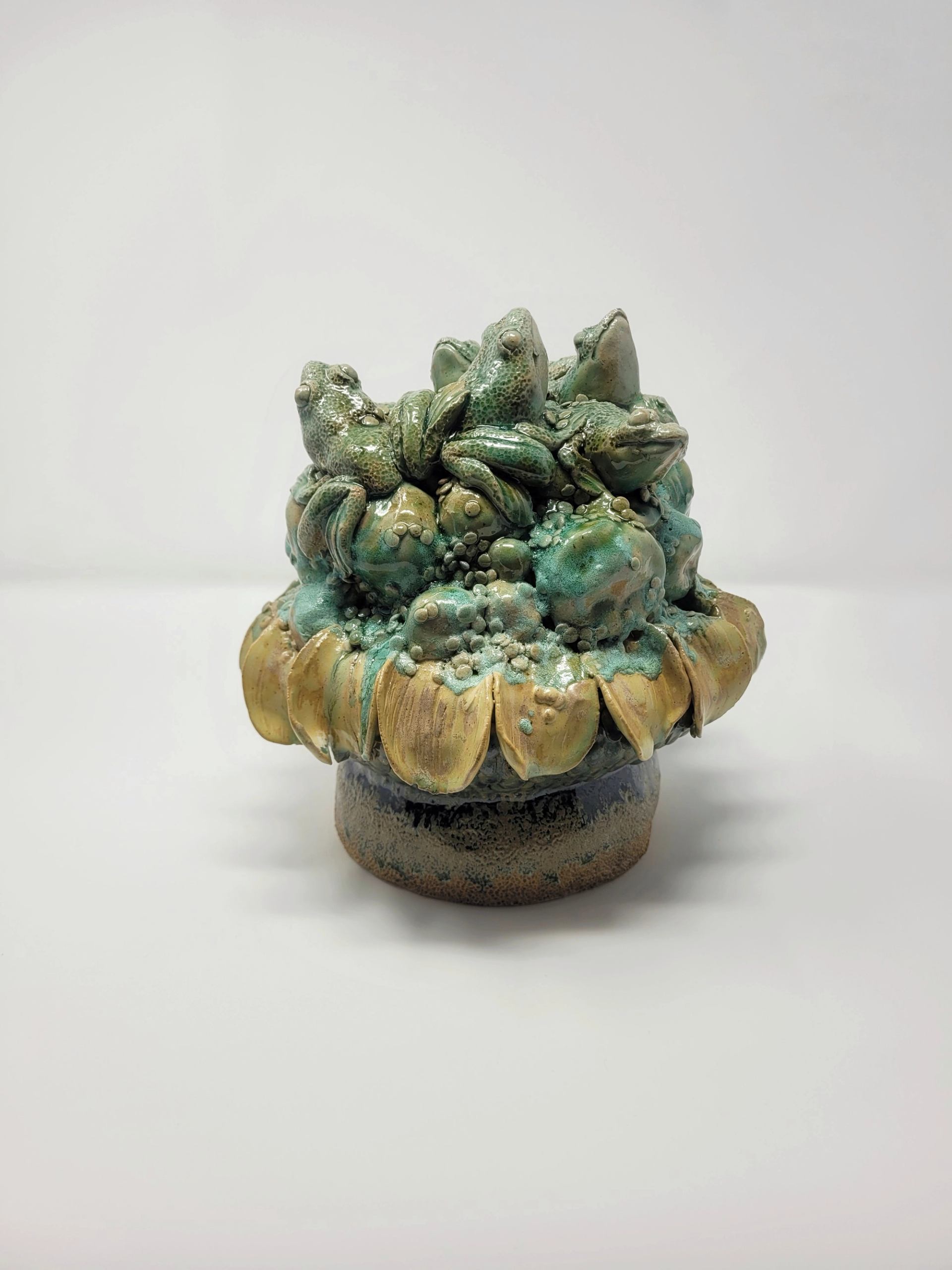 Ceramic sculpture of clustered frogs on textured base with yellow petal-like rim.
