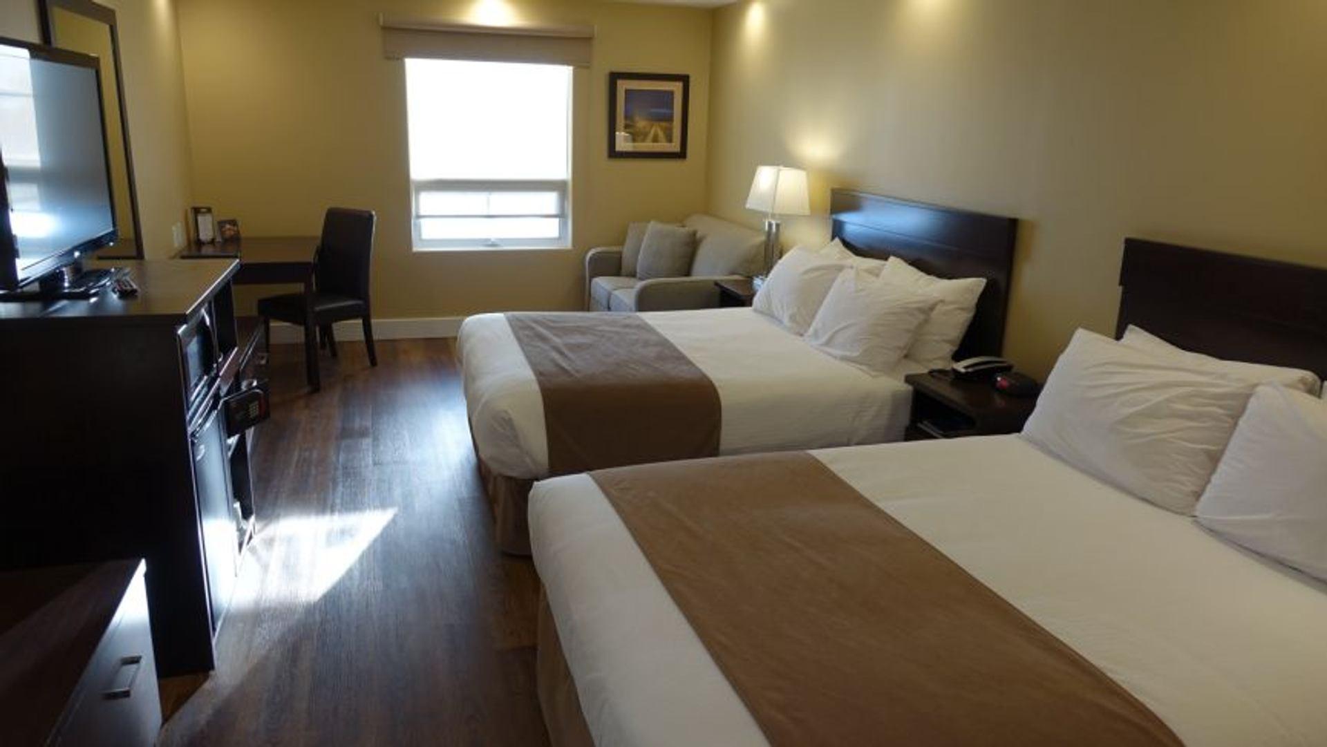 Hotel room with two double beds, desk, television, sofa and window with blind.