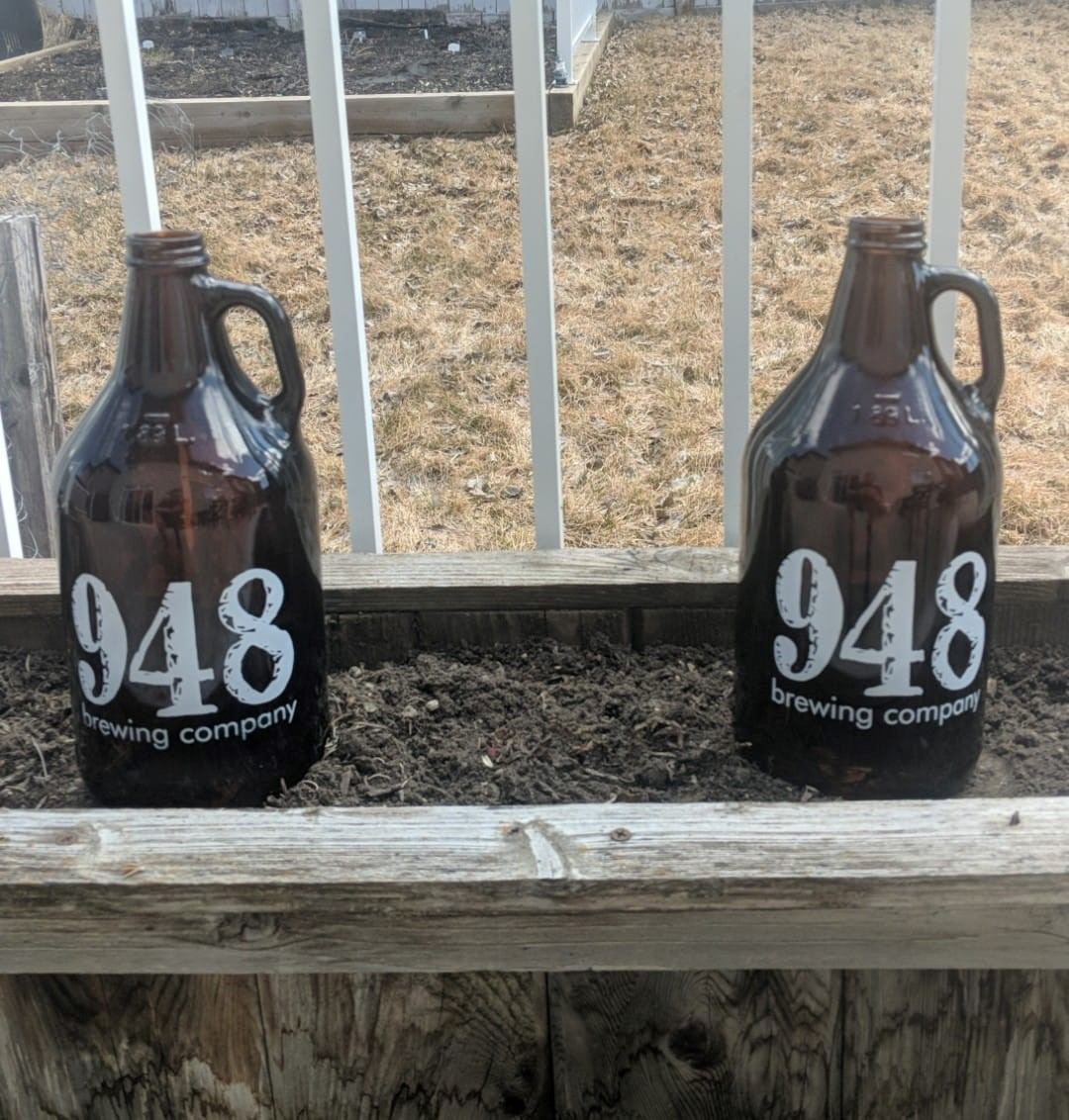 Two dark 948 Brewing Company bottles on a wooden railing, with grassy field beyond.