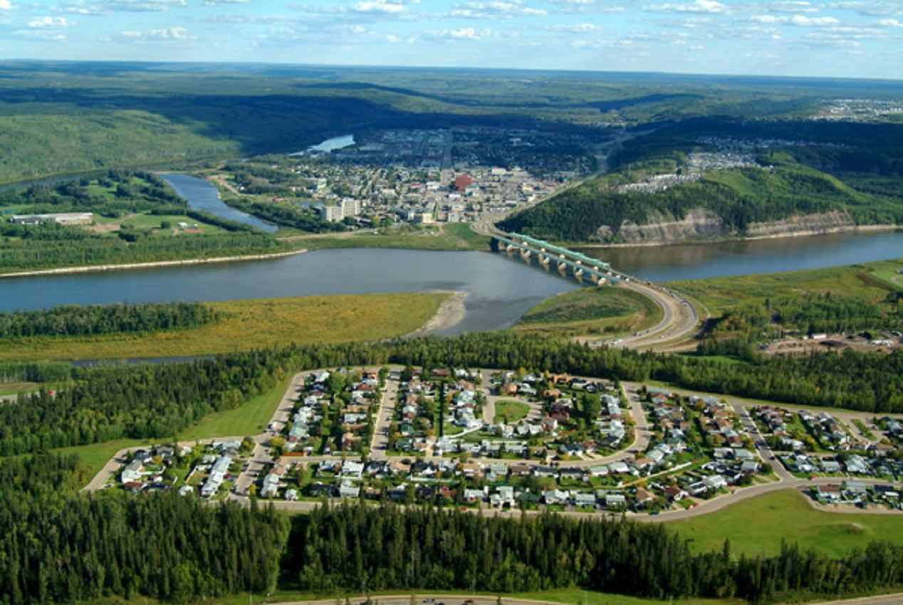 Aerial view of a riverside town with bridge, neighbourhood streets and surrounding forested hills.