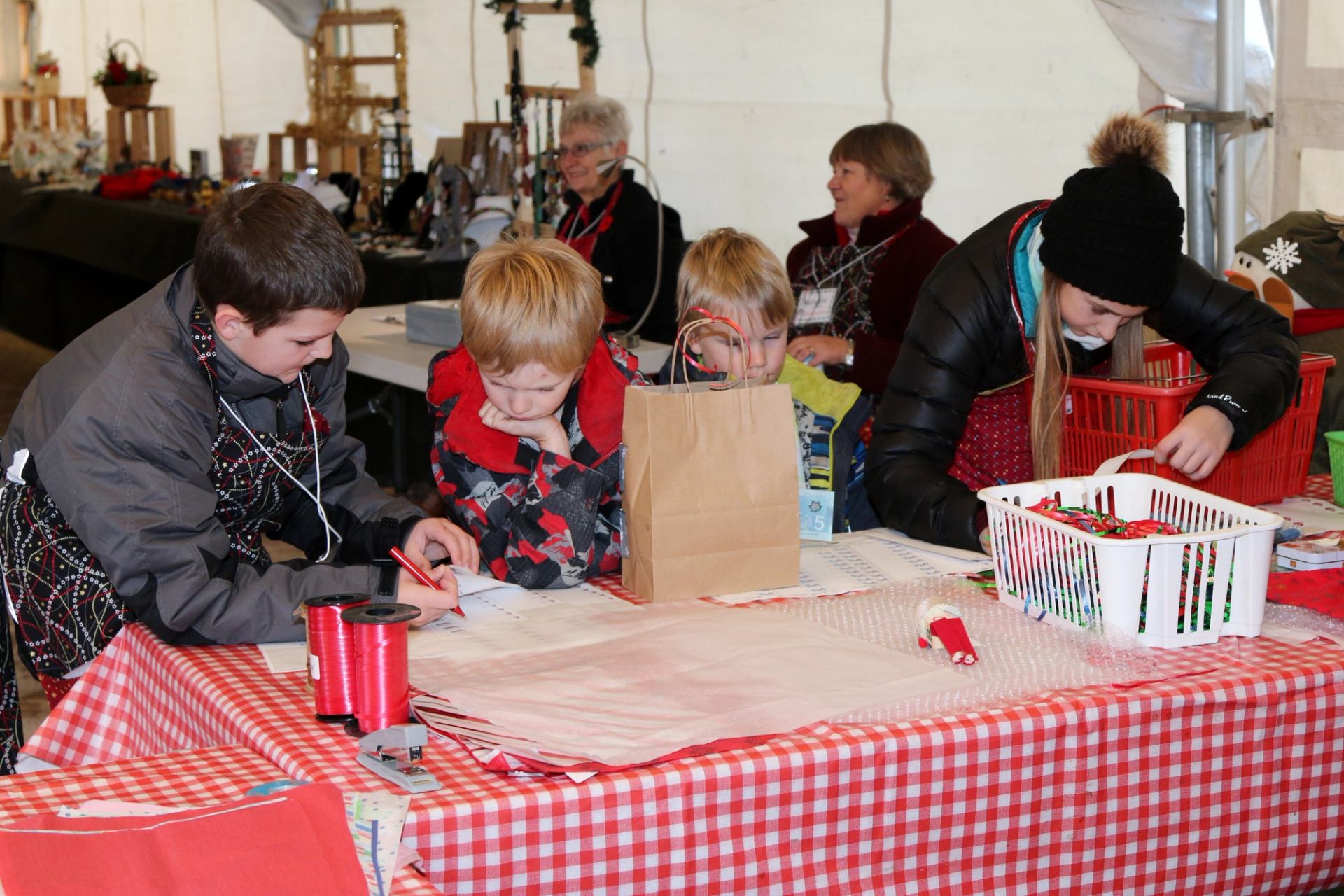People sit at a table wrapping gifts at Millarville Christmas Market under a tent.