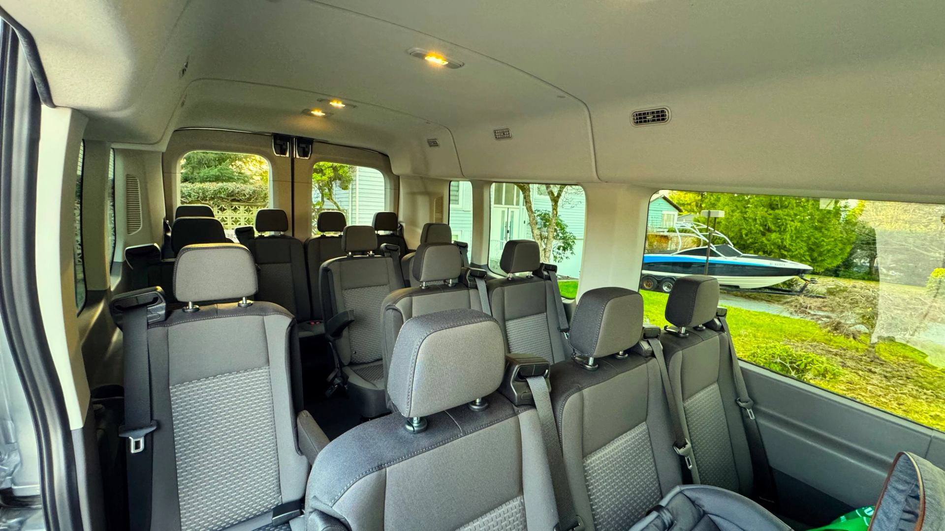 Interior of empty passenger van with grey seats and windows showing yard and boat.