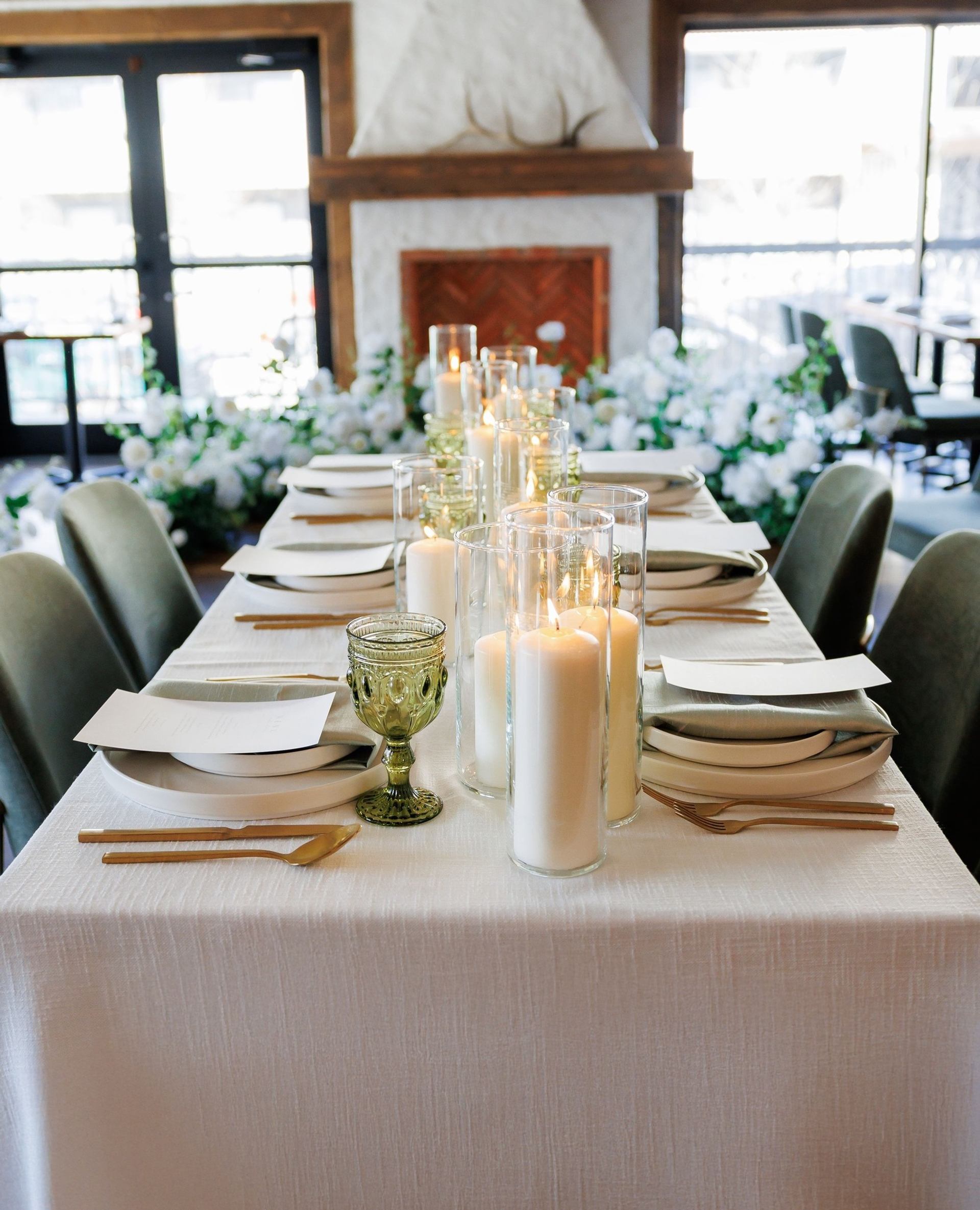 Elegant dining table with candles, gold cutlery, and floral fireplace backdrop.