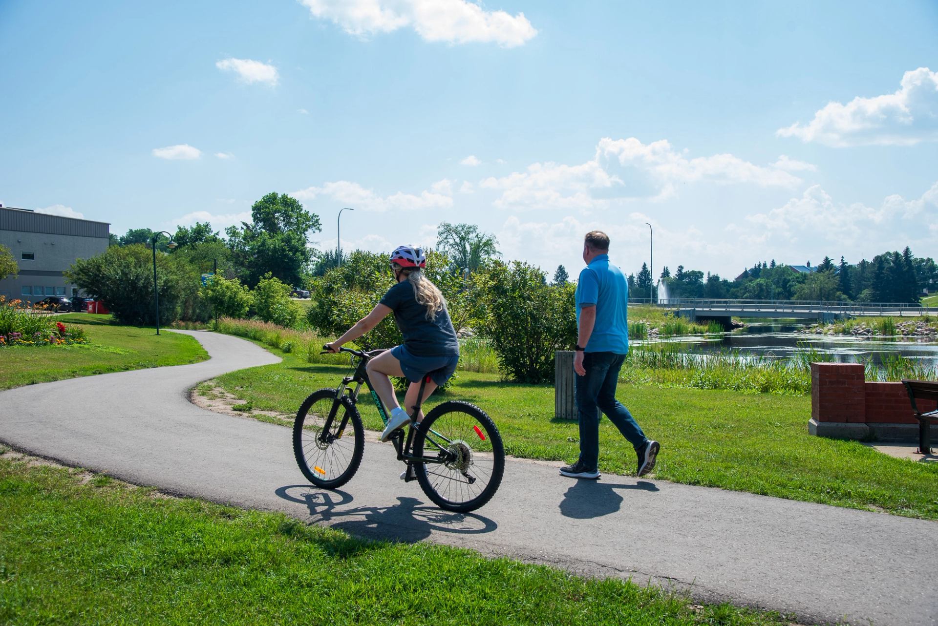 A person on a bike and a person walking share the trail as the bike passes the walker by Mirror Lake as they enjoy the sunshine.