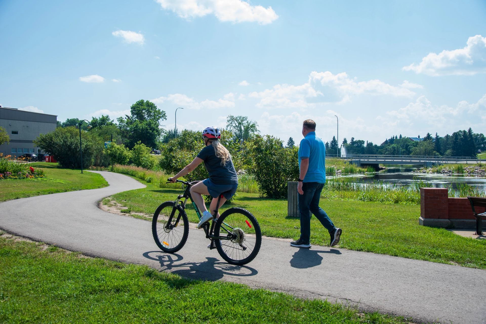 A person on a bike and a person walking share the trail as the bike passes the walker by Mirror Lake as they enjoy the sunshine.