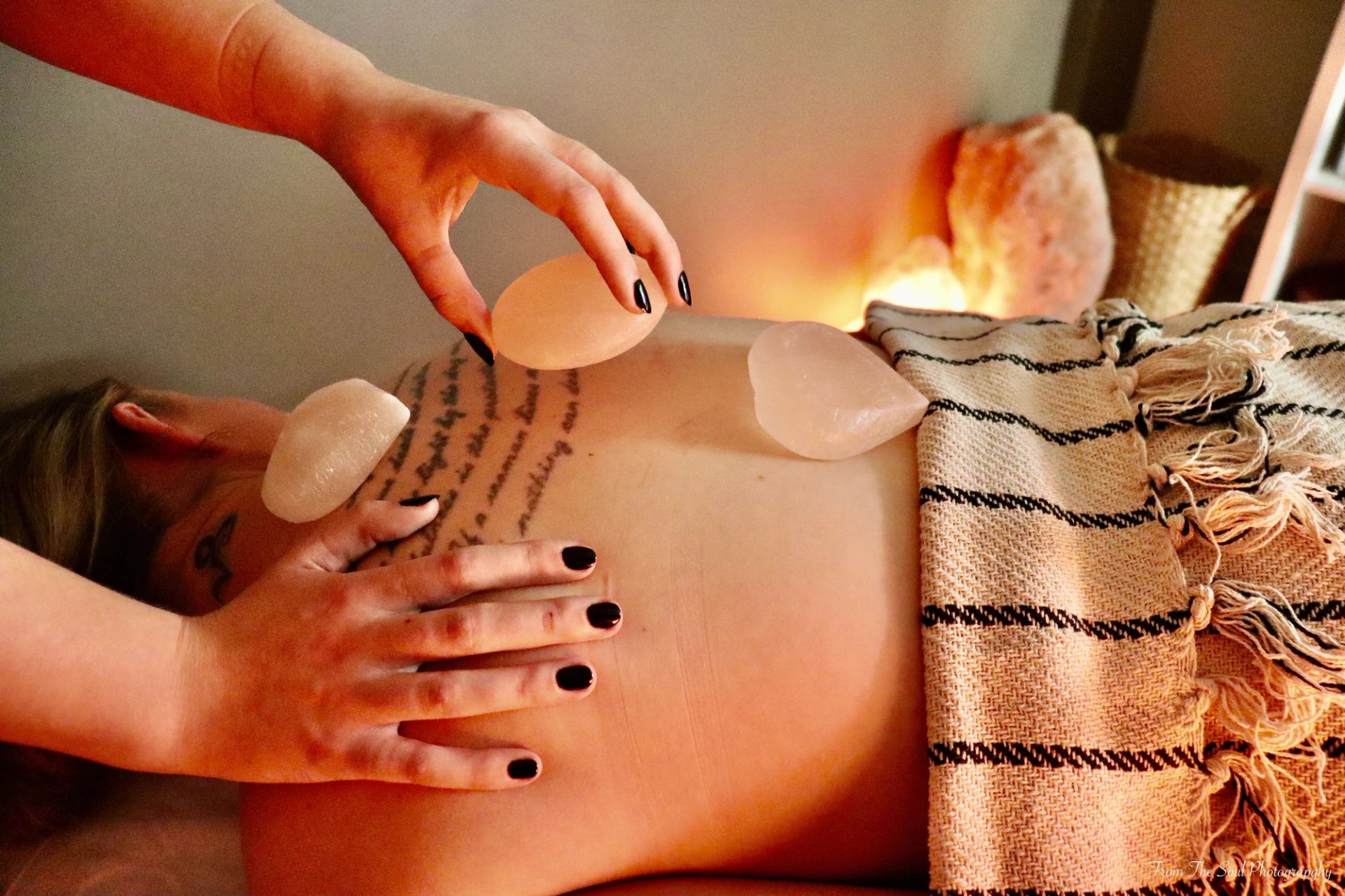 Hot stone massage in spa setting with warm lighting and striped blanket.