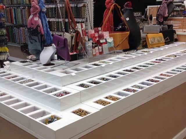 White display tables with open bins of beads, necklace busts, and hanging strands.
