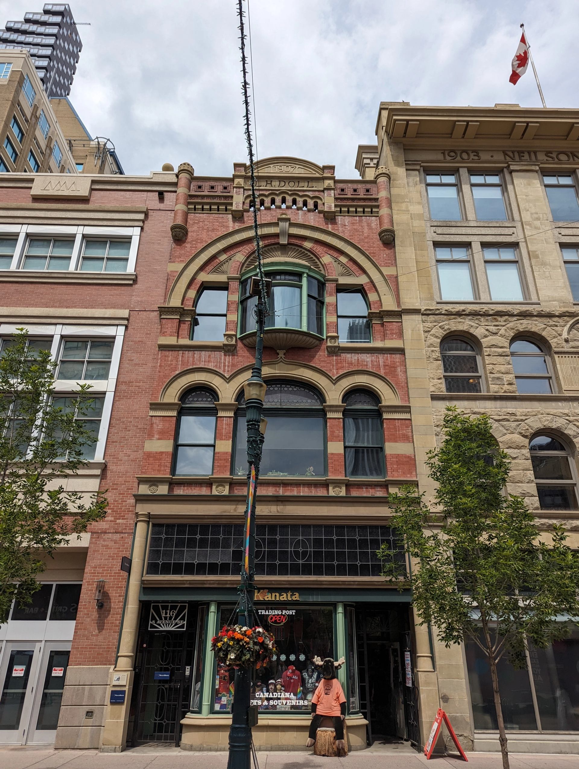Historic brick storefront with Kanata trading post sign, streetlamp, trees and Canadian flag.