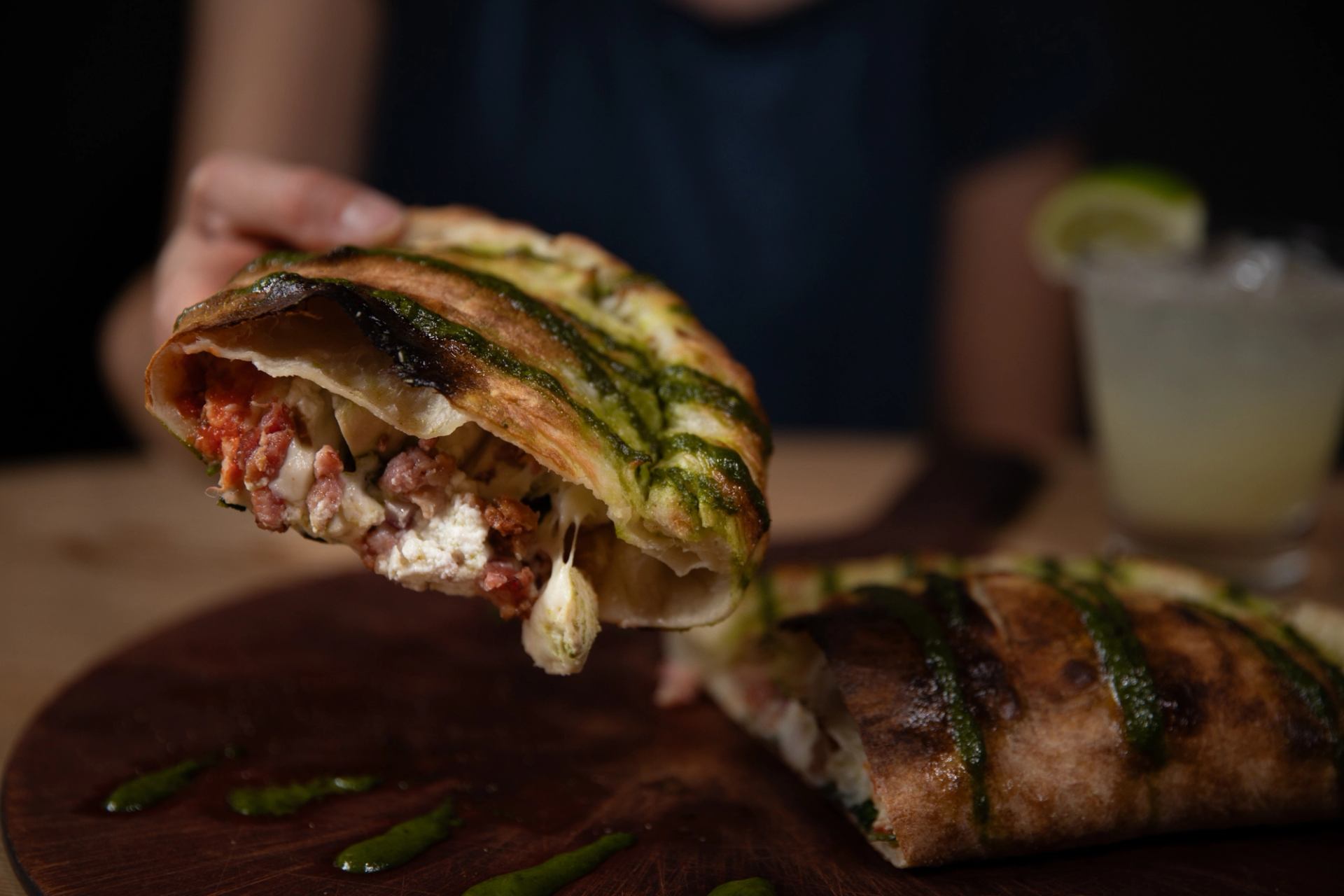 Stuffed flatbread pulled open with green pesto and meat filling on a wooden board.