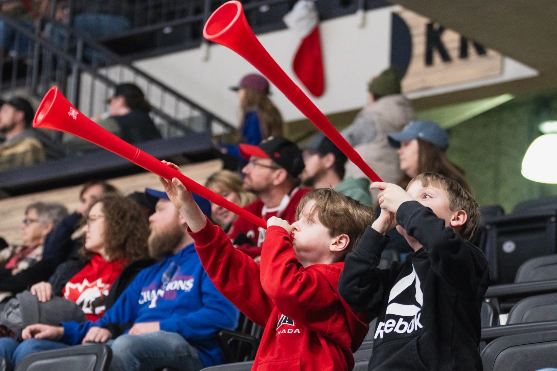 Children in team gear cheer from the stands, blowing red horns during a Red Deer Rebels home game.