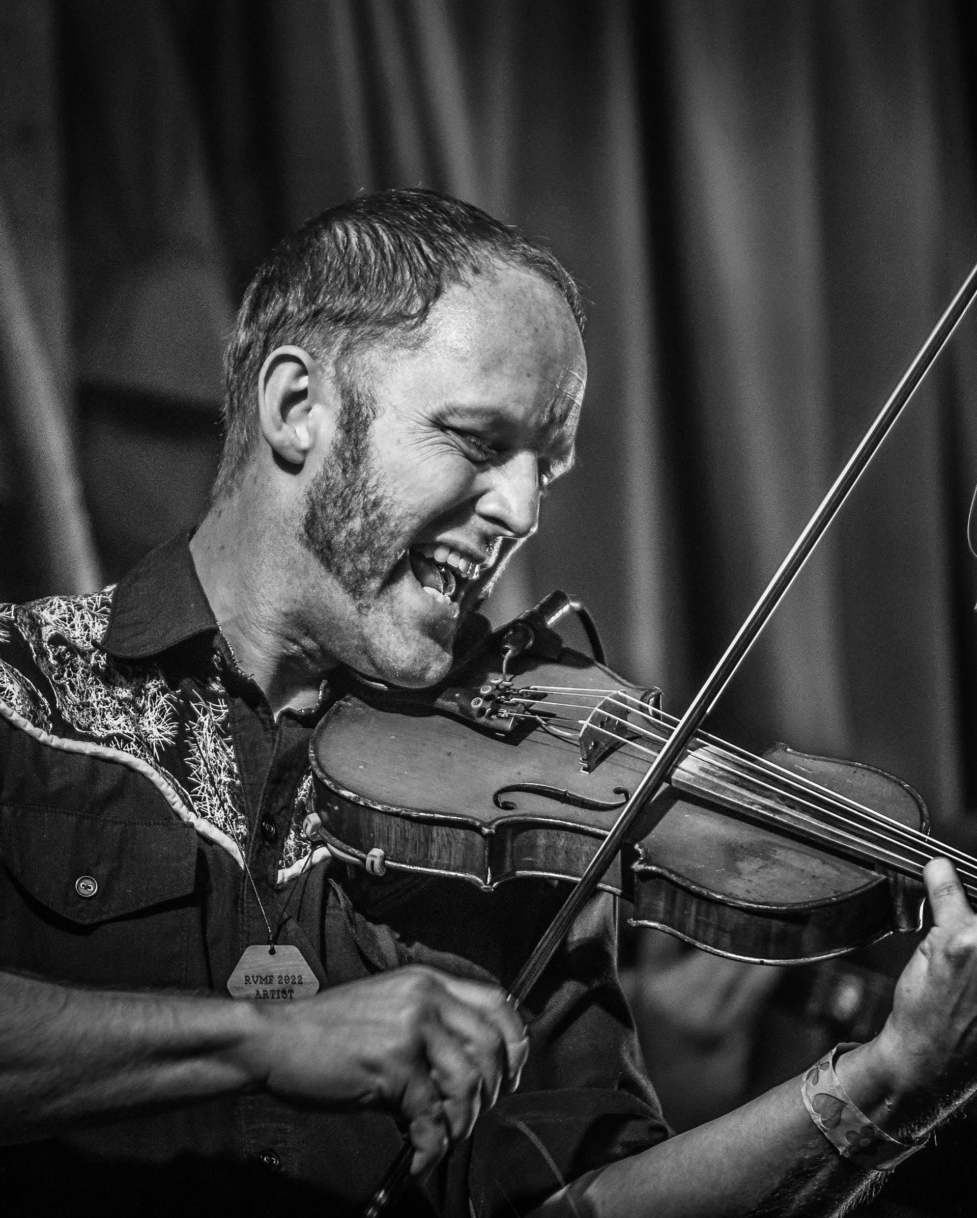 Black and white close-up of musician playing violin on stage with curtain backdrop.