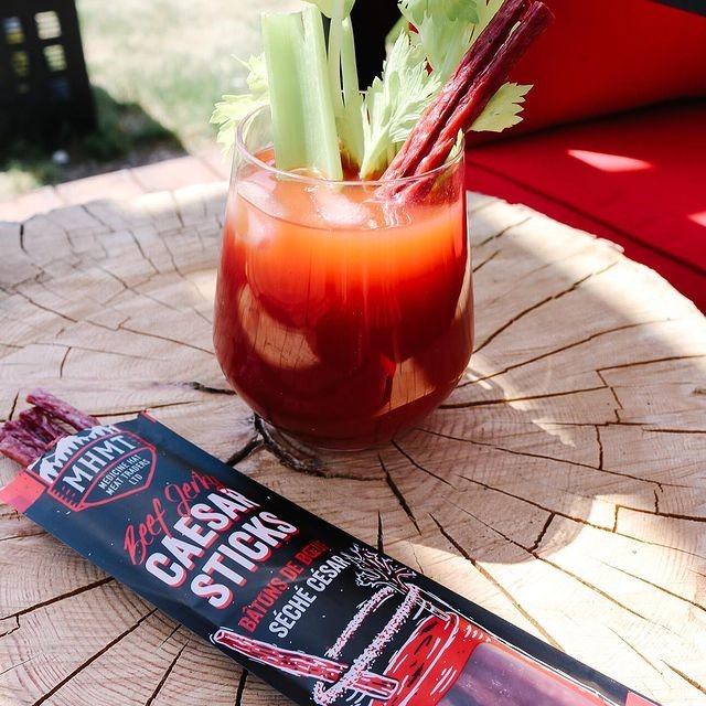 Caesar cocktail with celery and meat sticks on a wood table