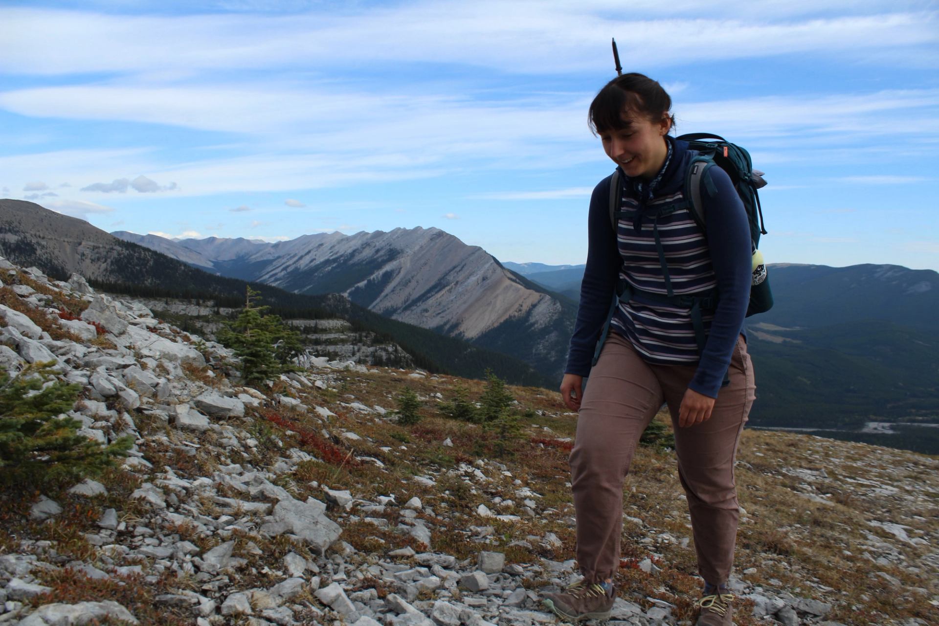 Hiker with backpack walking on rocky mountain trail with valley and peaks in view.