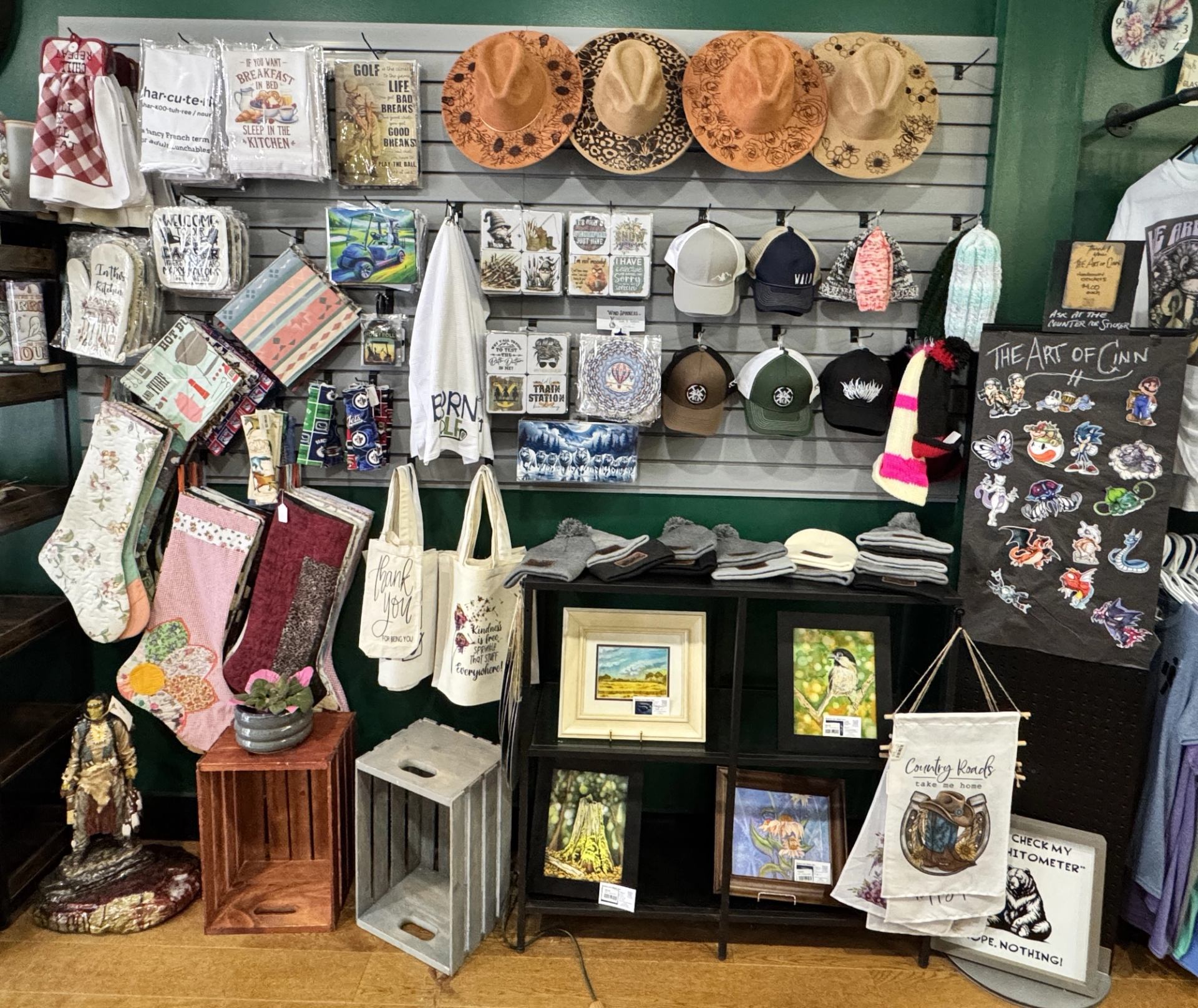 Display of hats, tote bags, socks, artwork, caps, textiles, and small gift items arranged on shelves and hooks.
