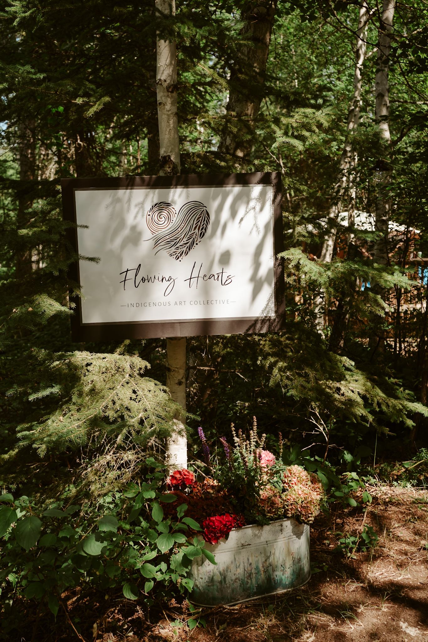 Flowing Hearts Indigenous Art Collective sign among trees and flowers.
