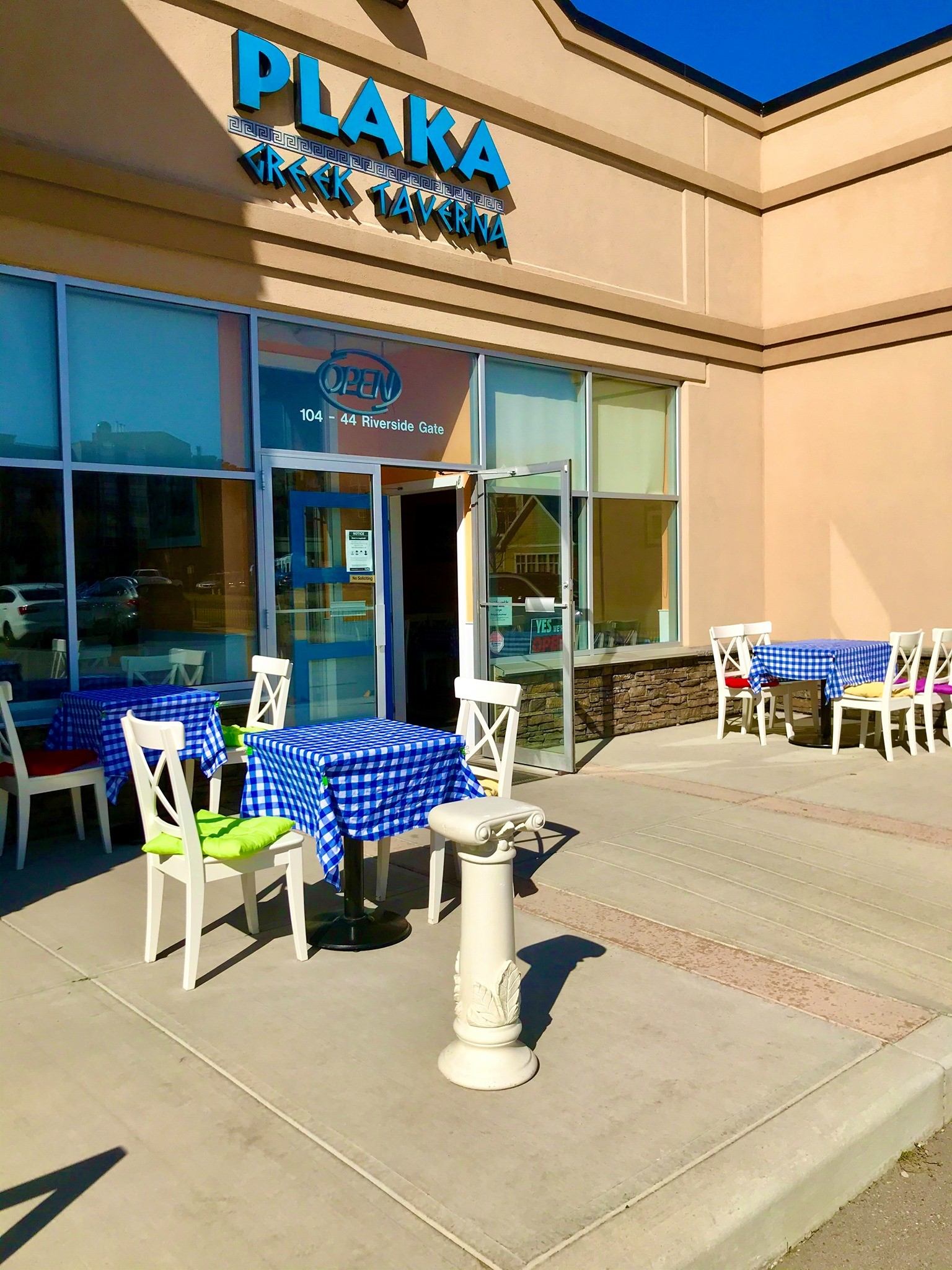 Exterior of Plaka Greek Kitchen with blue tablecloths and white column decor.