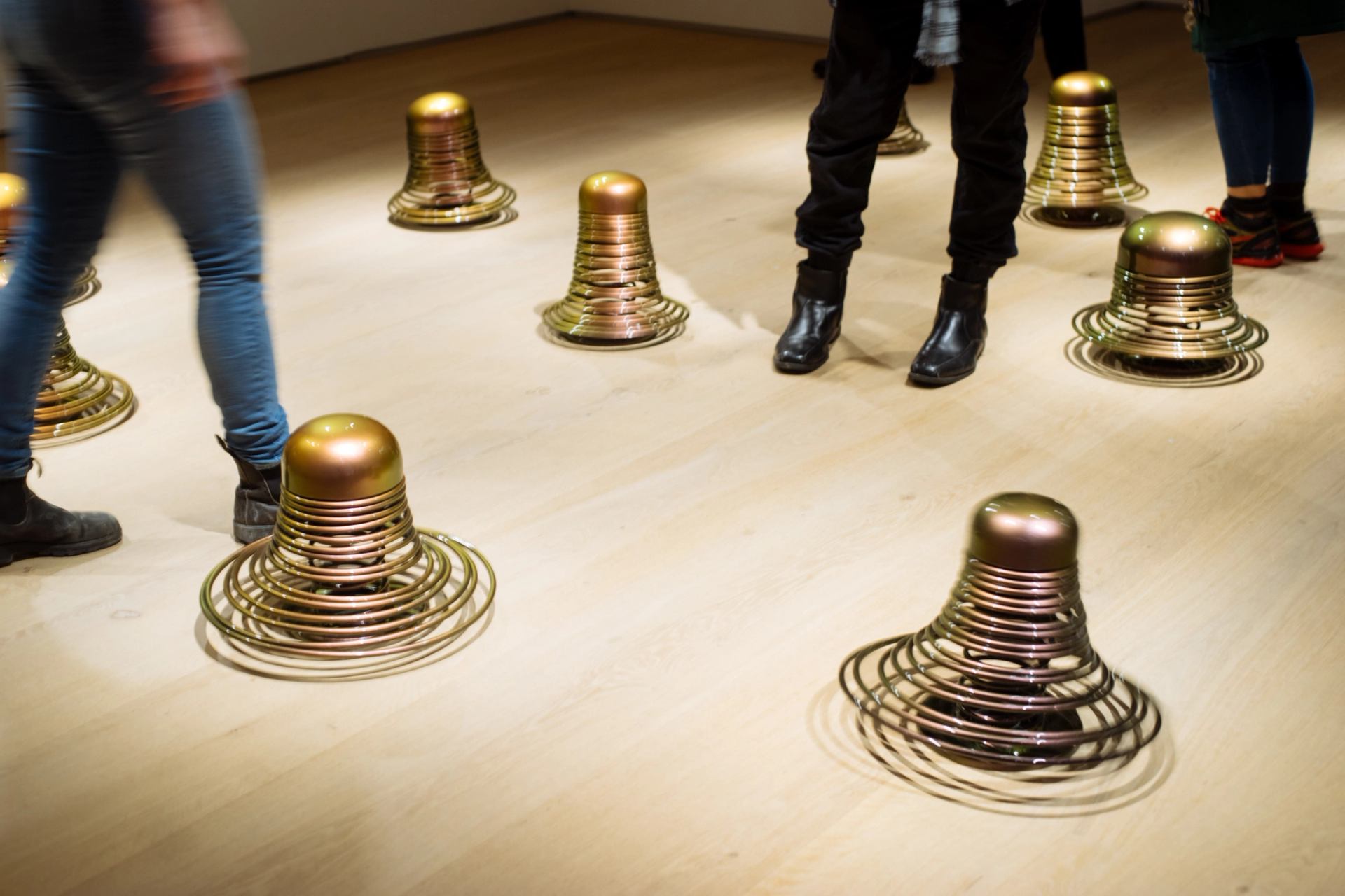 People walking around sculputes on a wooden floor.