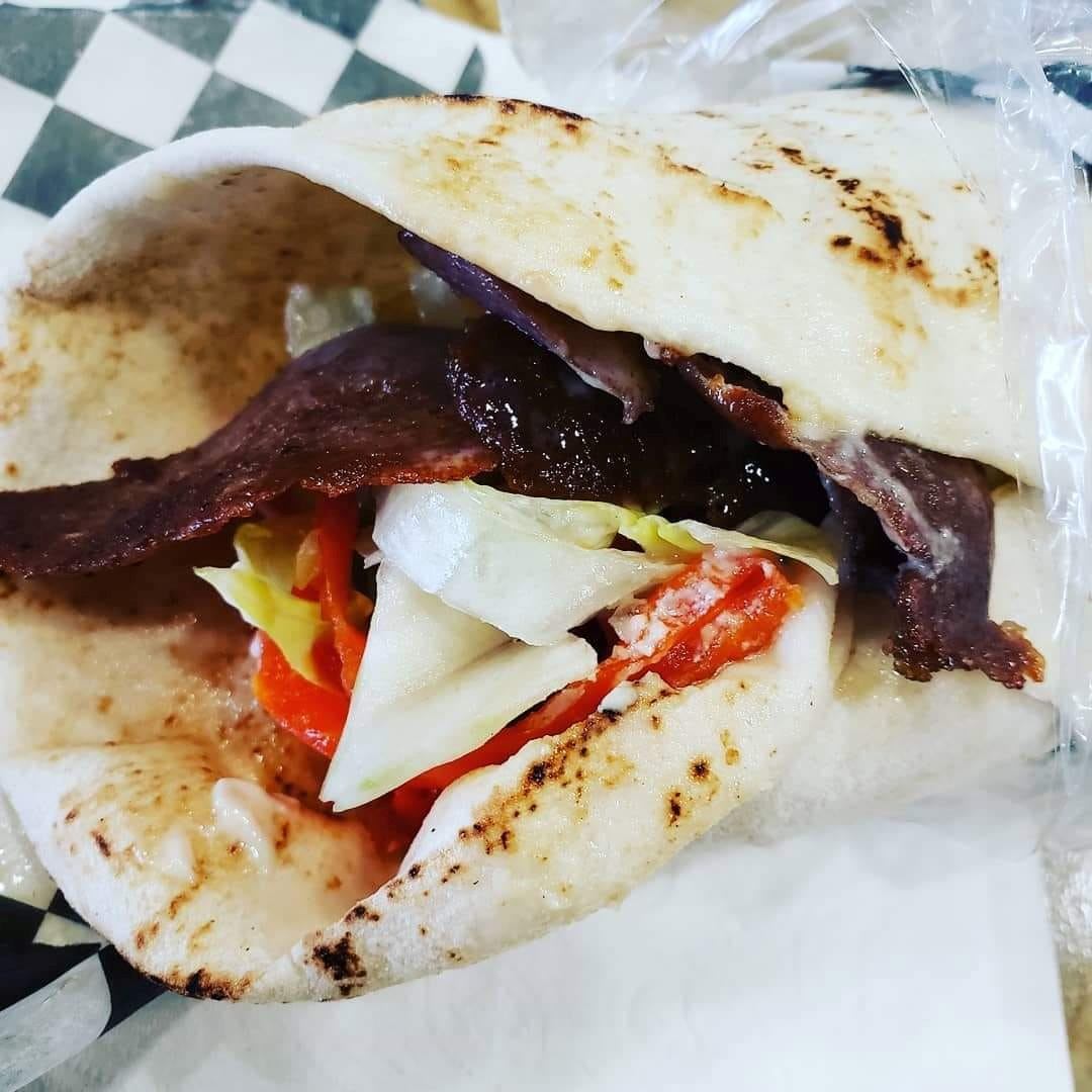 Sliced stuffed pita with melted cheese, bacon, and tomato on checkered tablecloth.