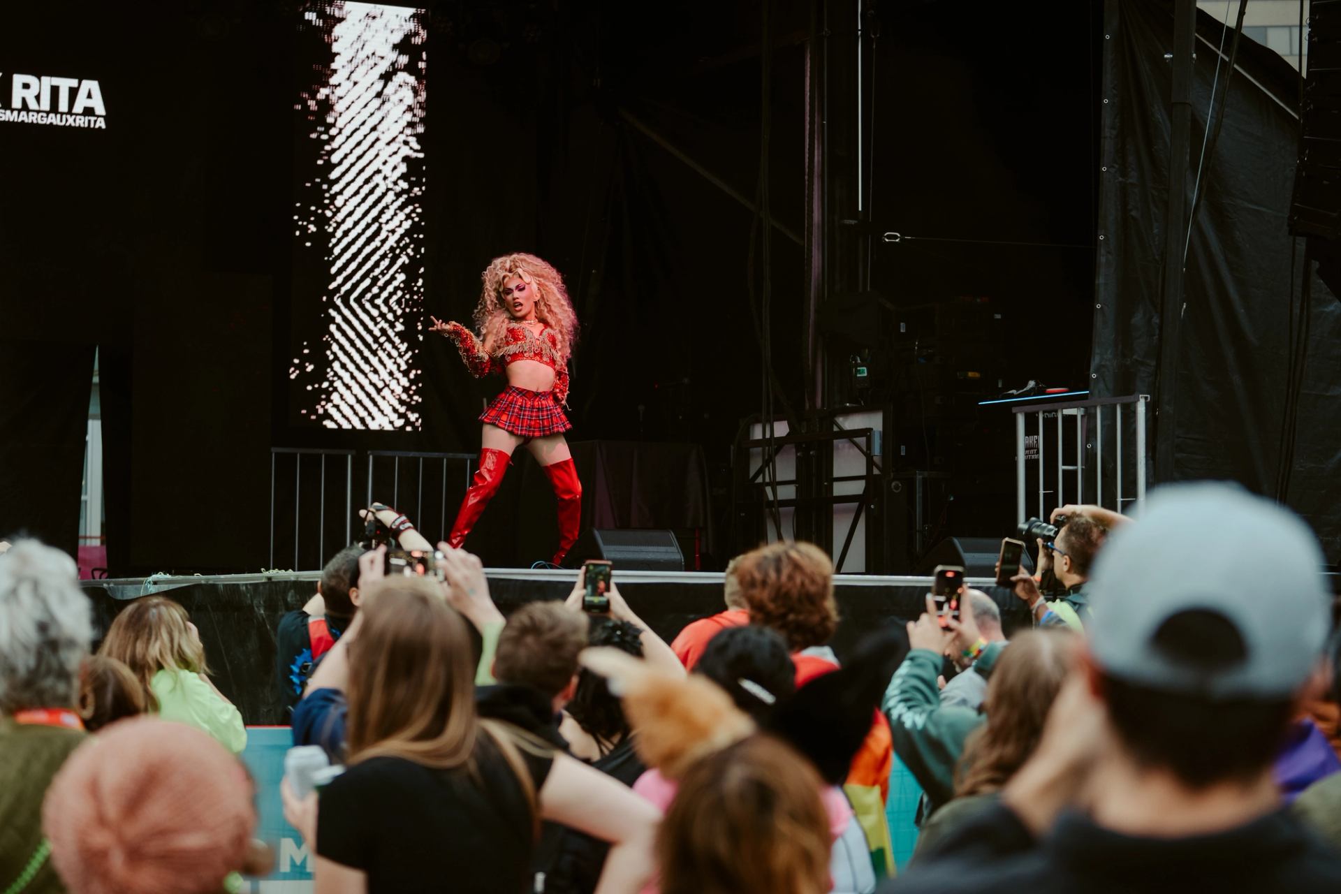 Performer in red outfit on stage as crowd records with phones.