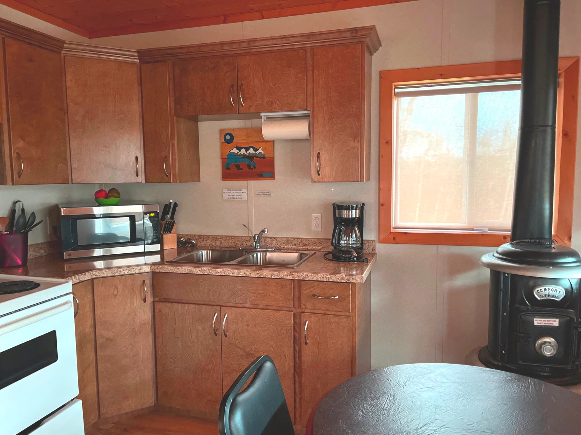 Compact kitchen with wooden cabinets, sink, microwave, and black wood-burning stove