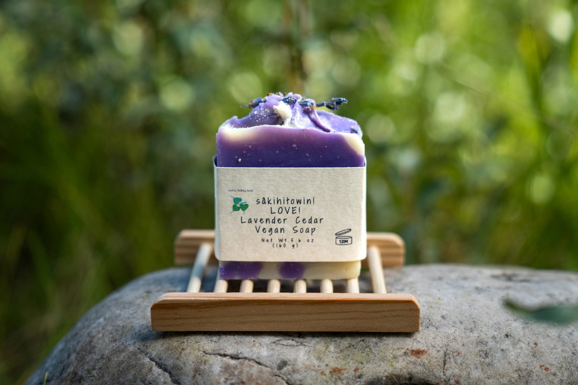 A lavender-colored soap bar rests on a wooden tray outdoors.