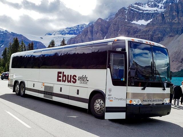 Ebus parked by lake with mountain and forest views.