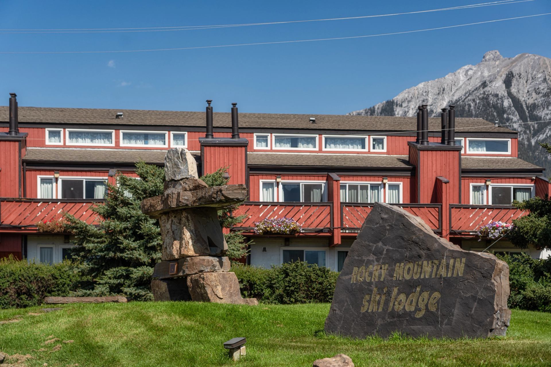 Red motel building with balconies, rock sculptures, and Rocky Mountains in the background.