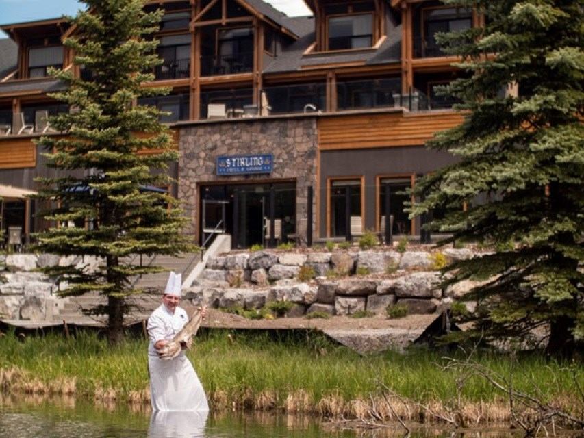Chef holding fish near pond outside Stirling building.