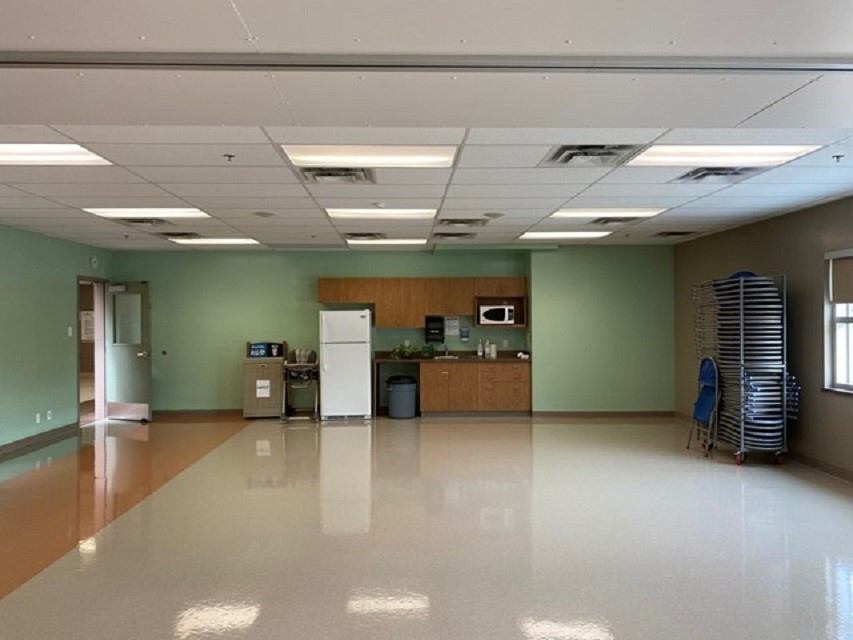 Recreation centre hallway with glossy floor, wood kitchenette, vending machine, and stacked chairs.