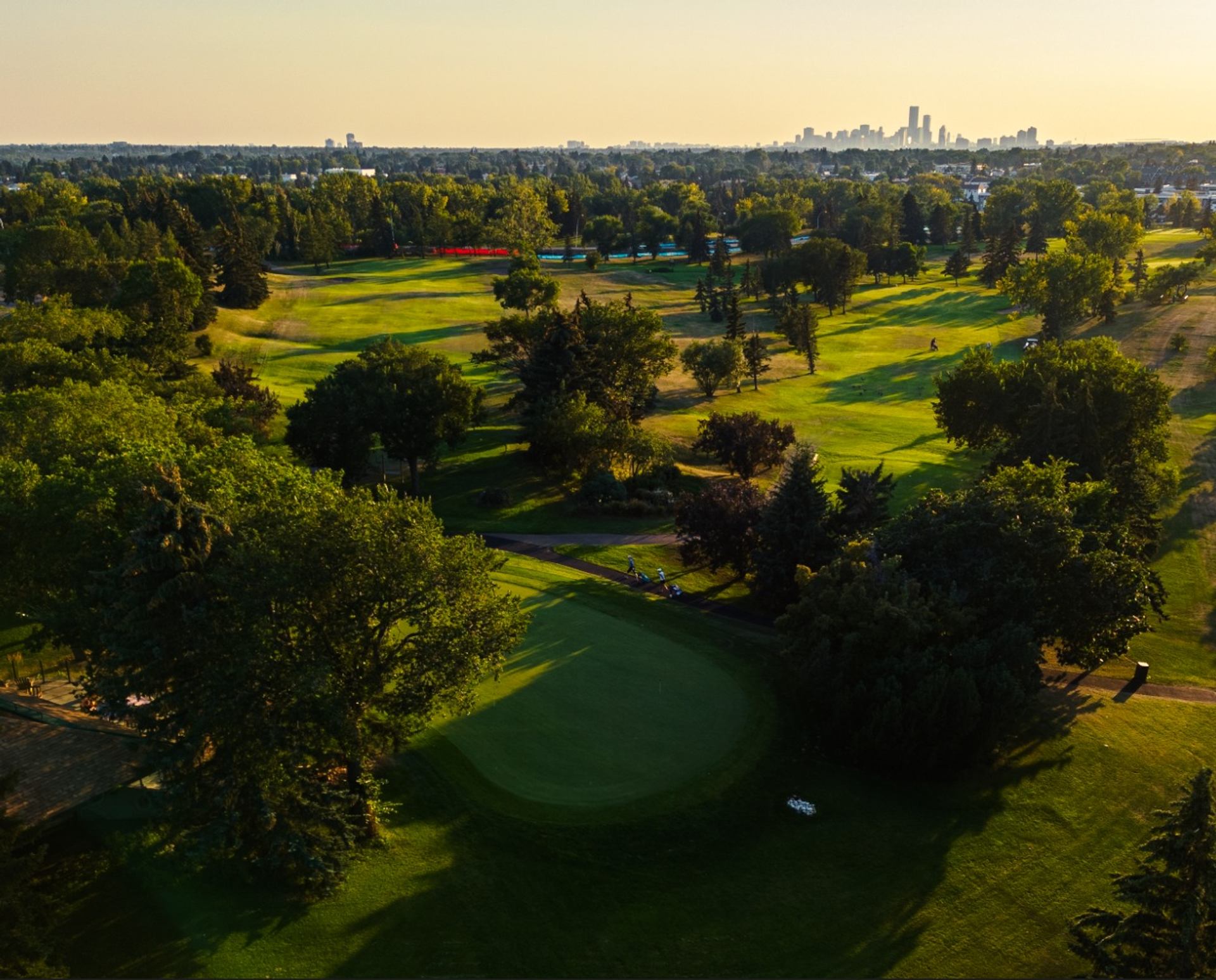 Aerial view of Rundle Park Golf Course with rolling fairways, trees, and city skyline.