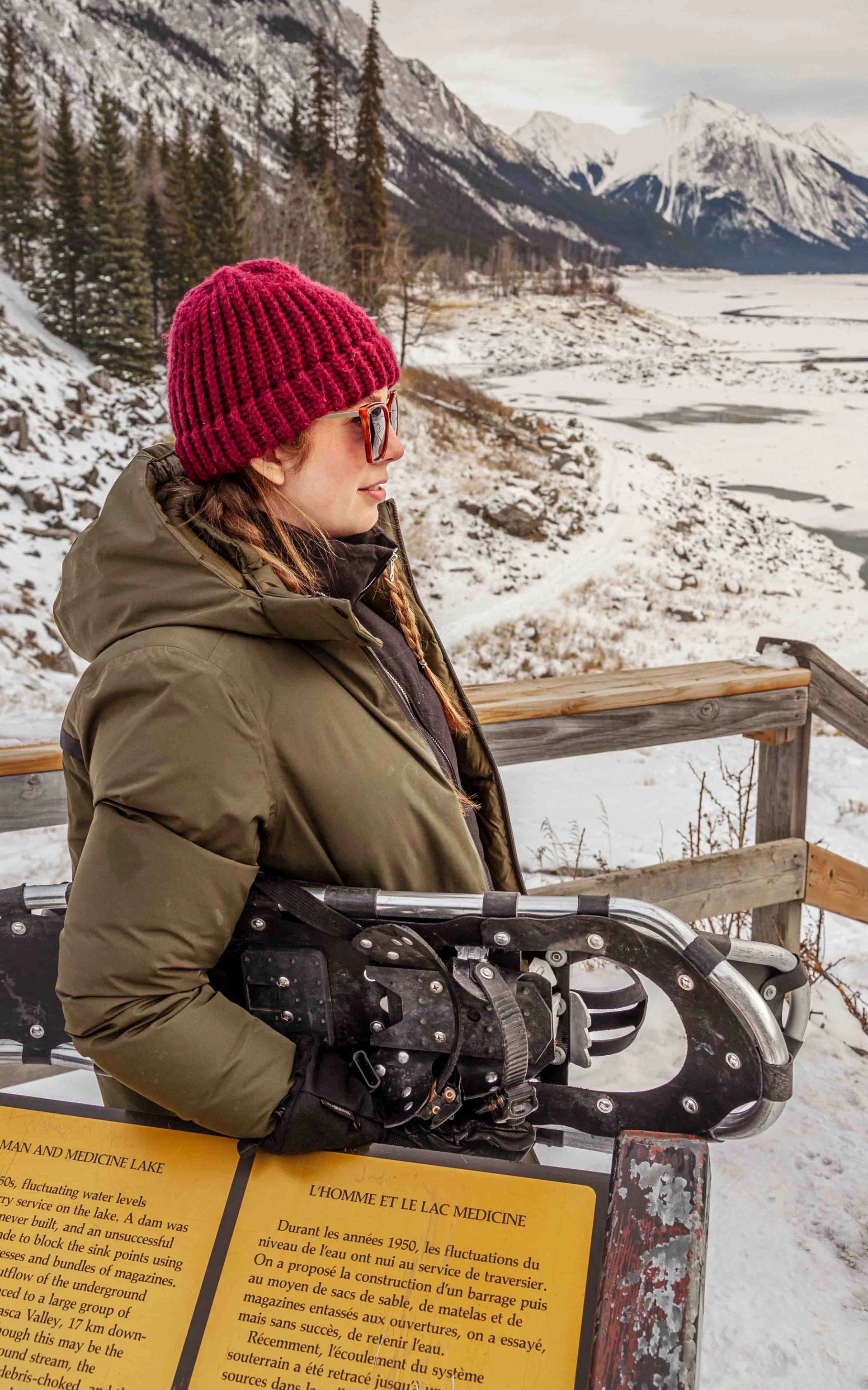 Woman in red toque on snowshoe tour platform overlooking snowy mountain lake in Jasper.