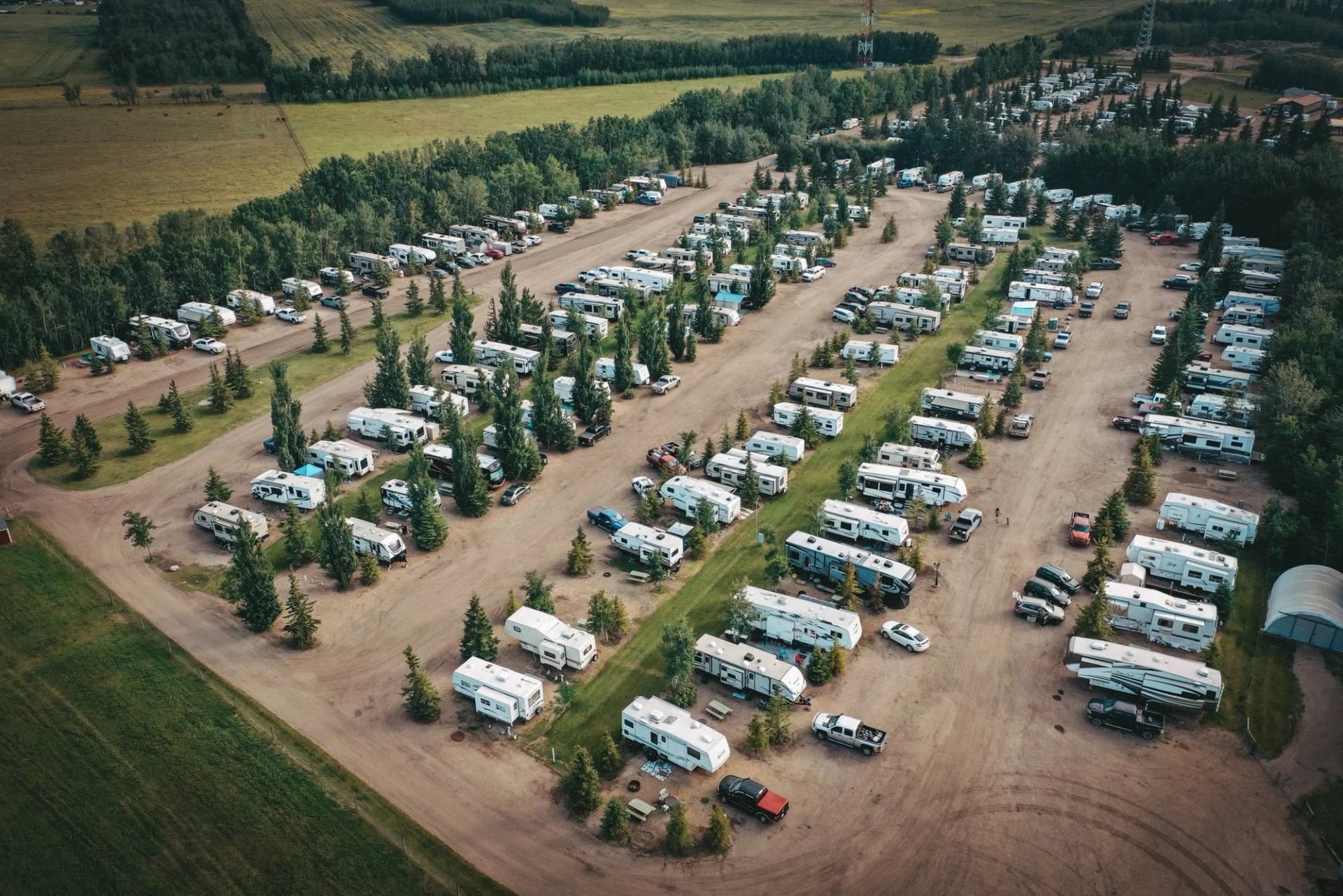 Aerial view of a large RV park with trailers, vehicles and trees in rows.