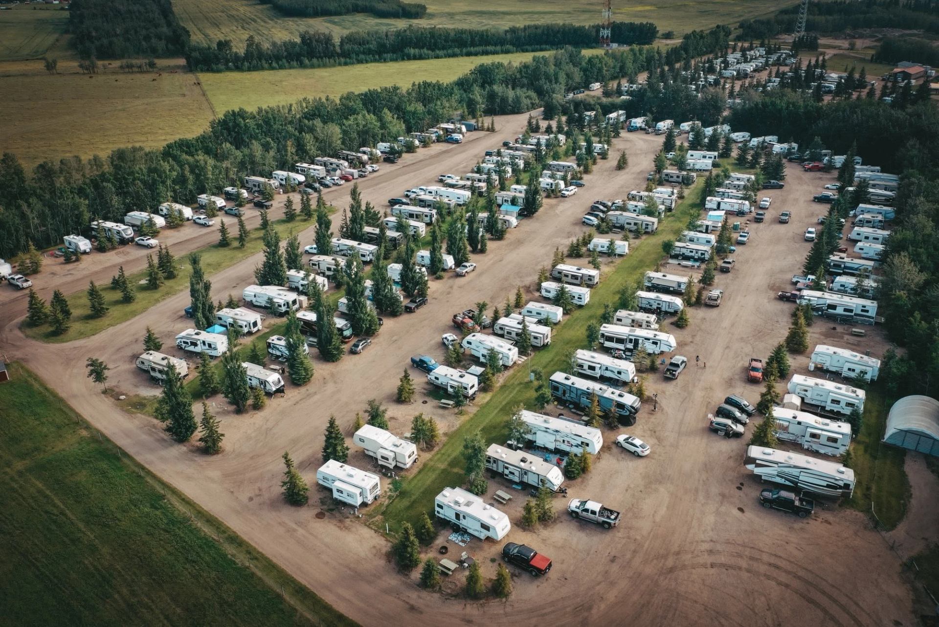 Aerial view of a large RV park with trailers, vehicles and trees in rows.
