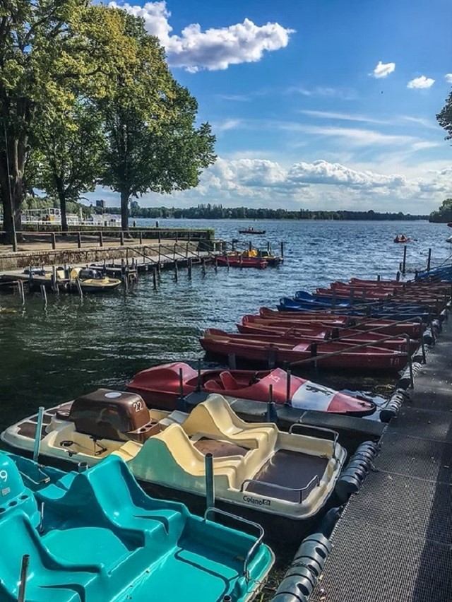 Colorful pedal boats docked by a lake under a partly cloudy sky with trees nearby.