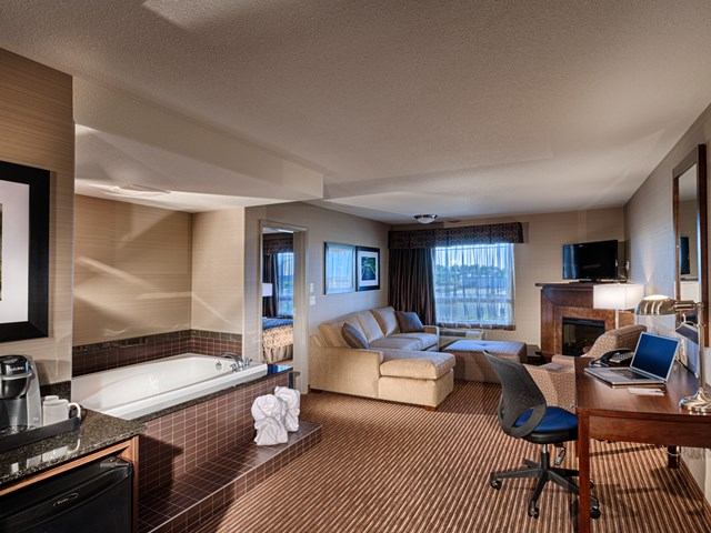 Hotel suite with sofa, desk, TV, and in-room whirlpool tub at Canalta Lac La Biche.
