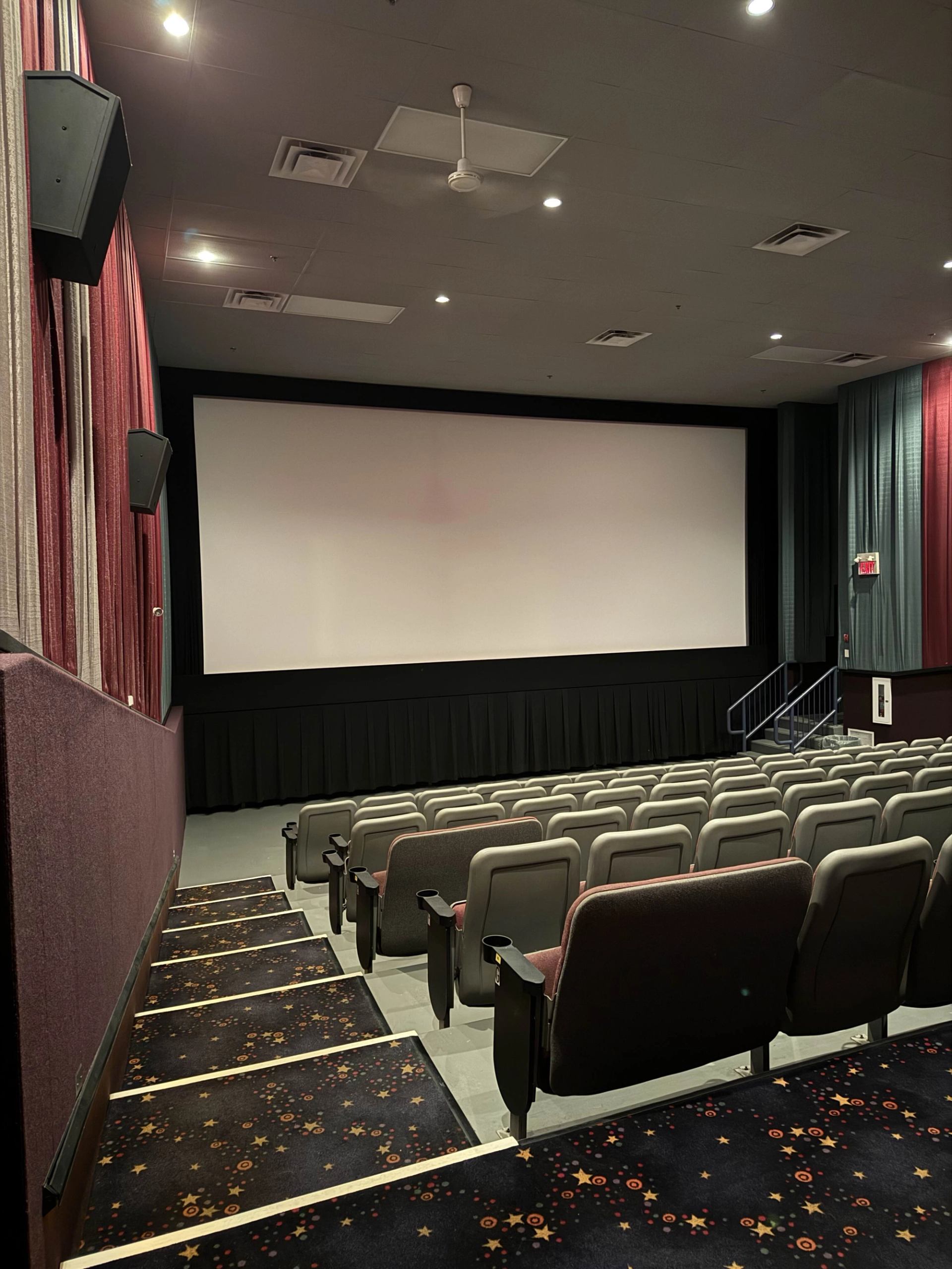 Empty movie theater with rows of seats facing a large screen and dim lighting.