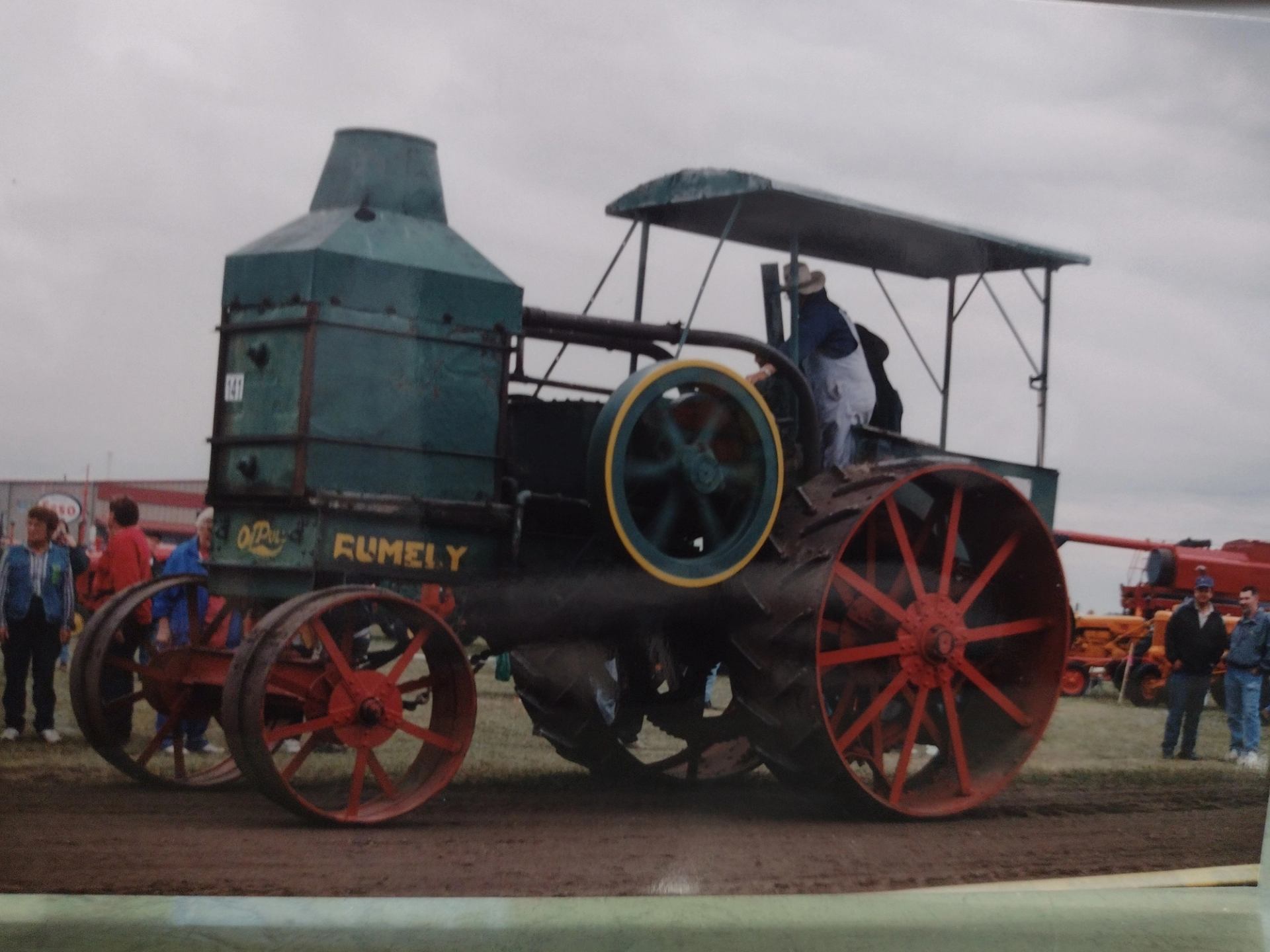 People stand near a classic, steam powered tractor.