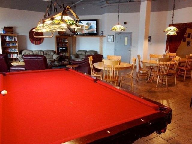 Game room with red pool table, leather sofas, and round wooden tables under hanging lights.