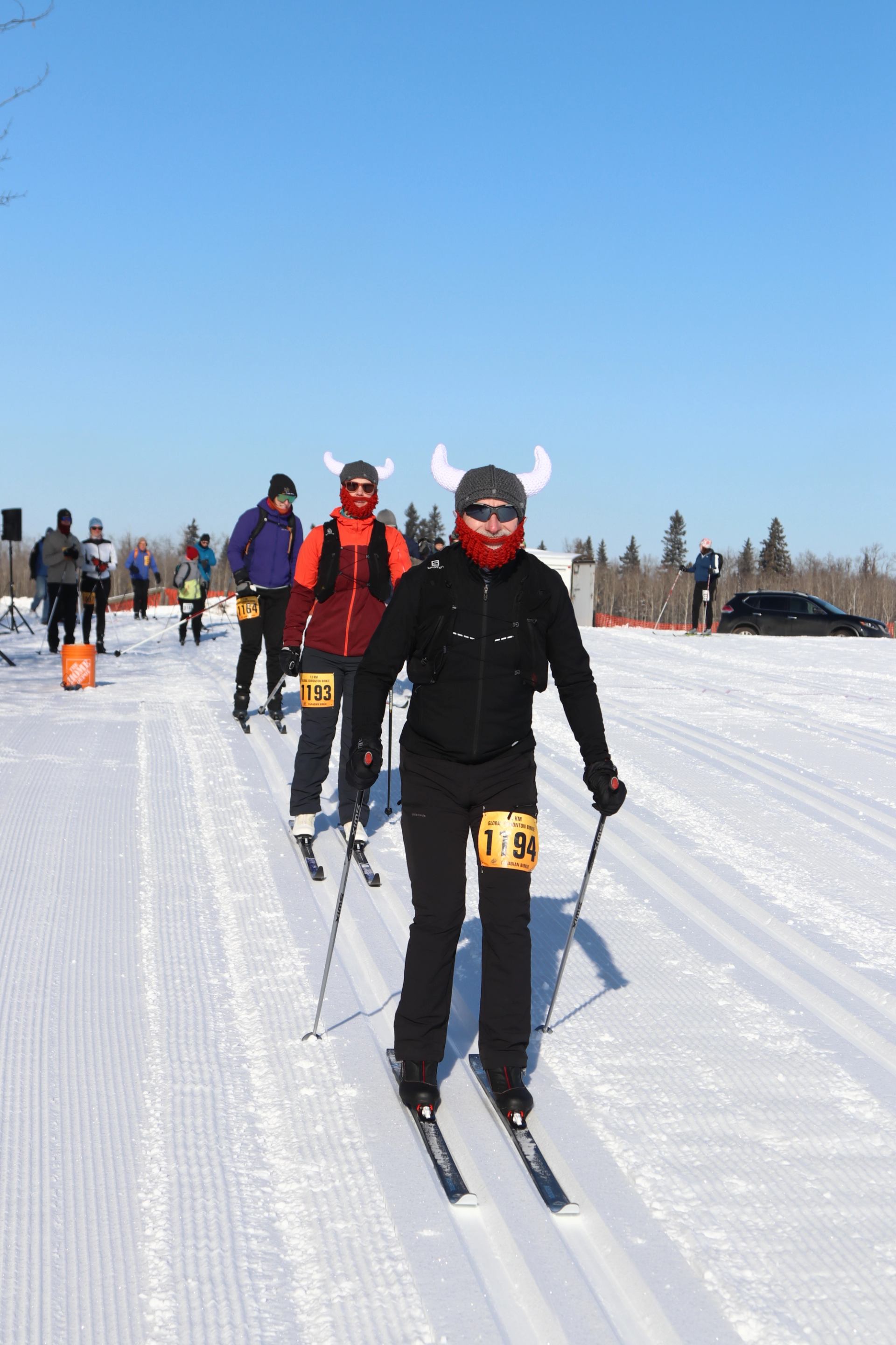 Skiers race on a snowy trail under clear blue skies at the Canadian Birkie Festival.