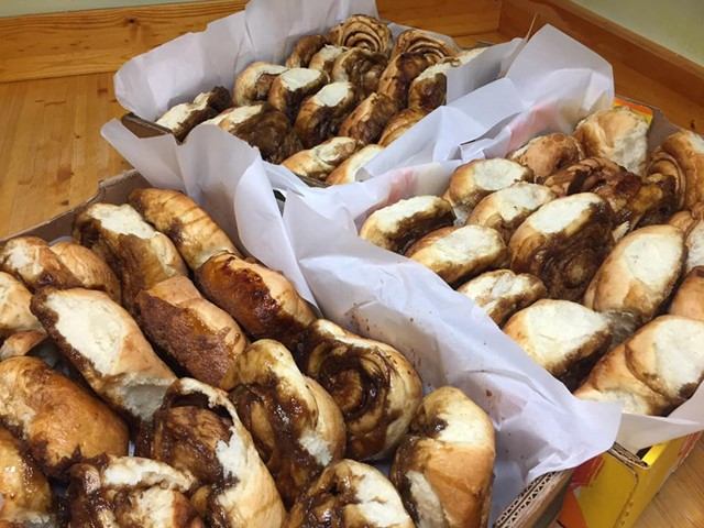 Pastries in trays, including cinnamon rolls and danish with powdered sugar on top.