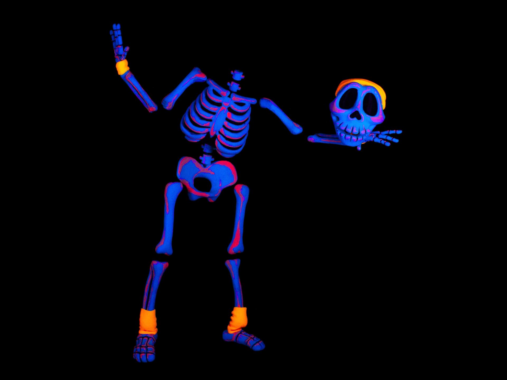 Neon blue skeleton with detached skull and orange accessories on black background.
