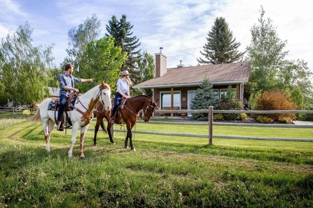 Two people riding horses in front of the Rocking R Guest Ranch.